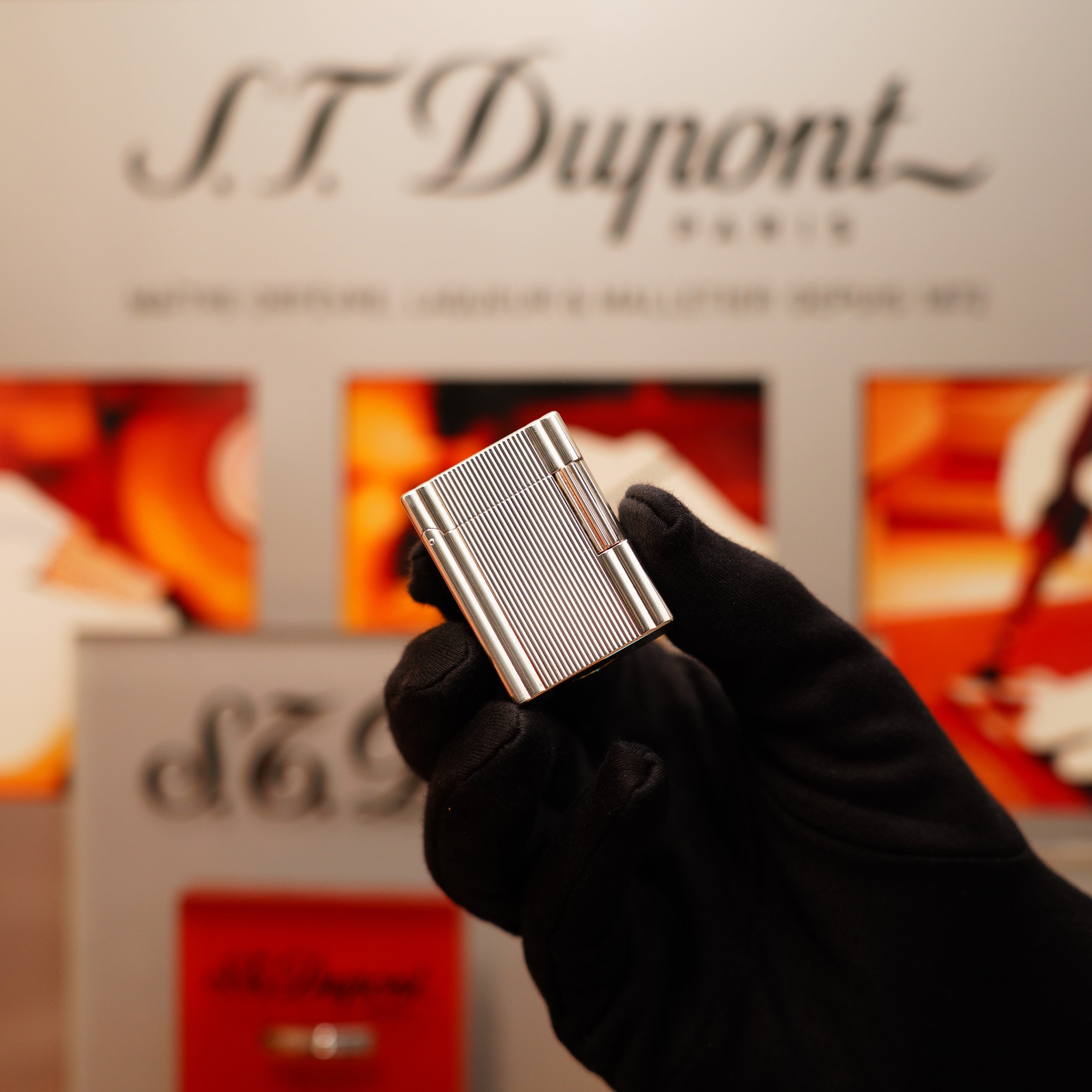 A gloved hand holds a Vintage 2000 S.T. Dupont Heavy Silver Finish Small Ligne 1 Vertical Ligne lighter, with the S.T. Dupont branding in the background.