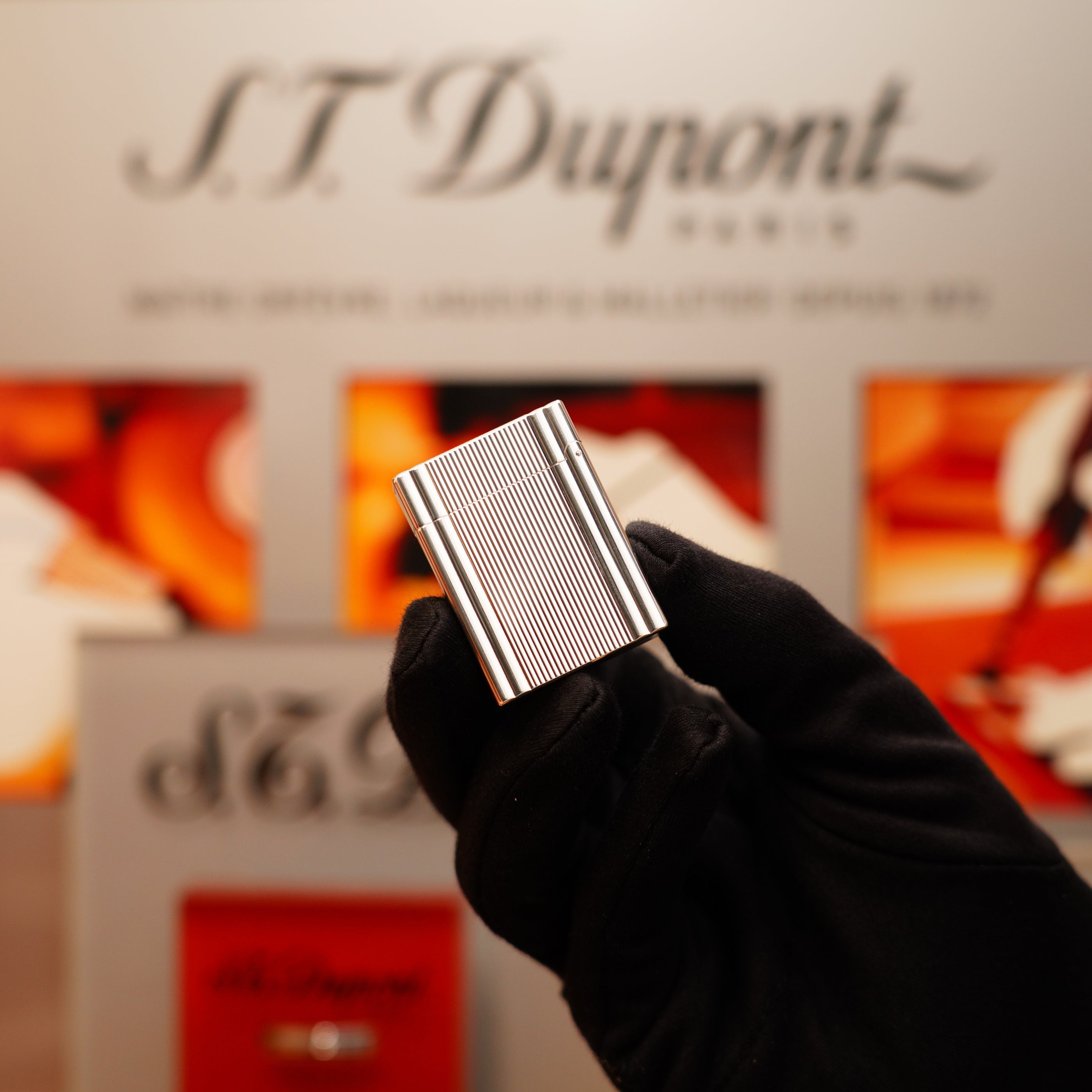 A gloved hand holding a Vintage 2000 S.T. Dupont Silver Finish Ligne 1 Lighter with a vertical line design in front of a blurred display background.