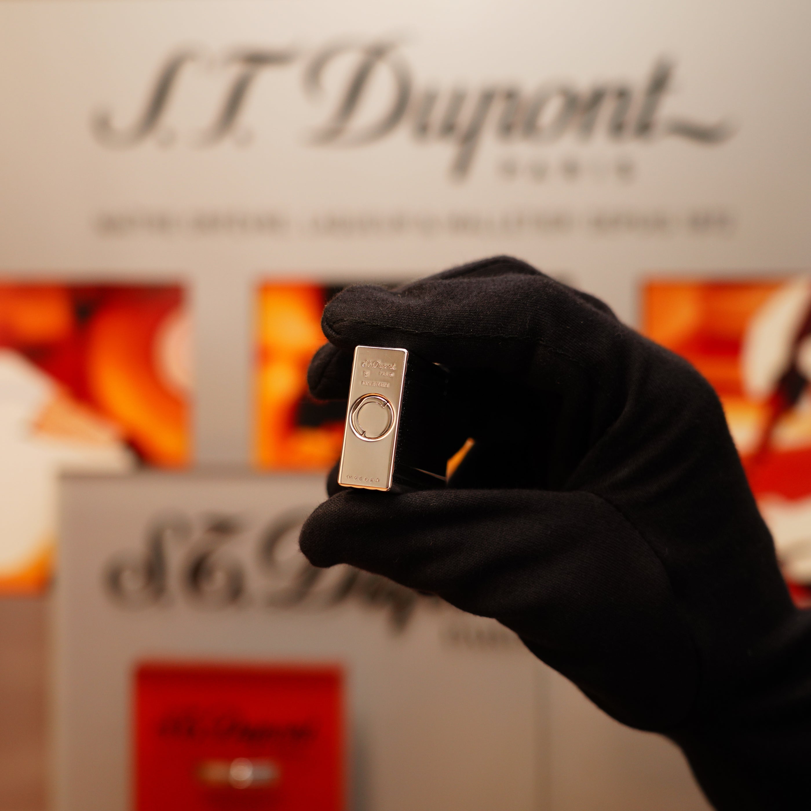 A gloved hand holds a Vintage 2000 S.T. Dupont Ligne 1 lighter with a heavy silver finish against a blurred backdrop of the brand's name.