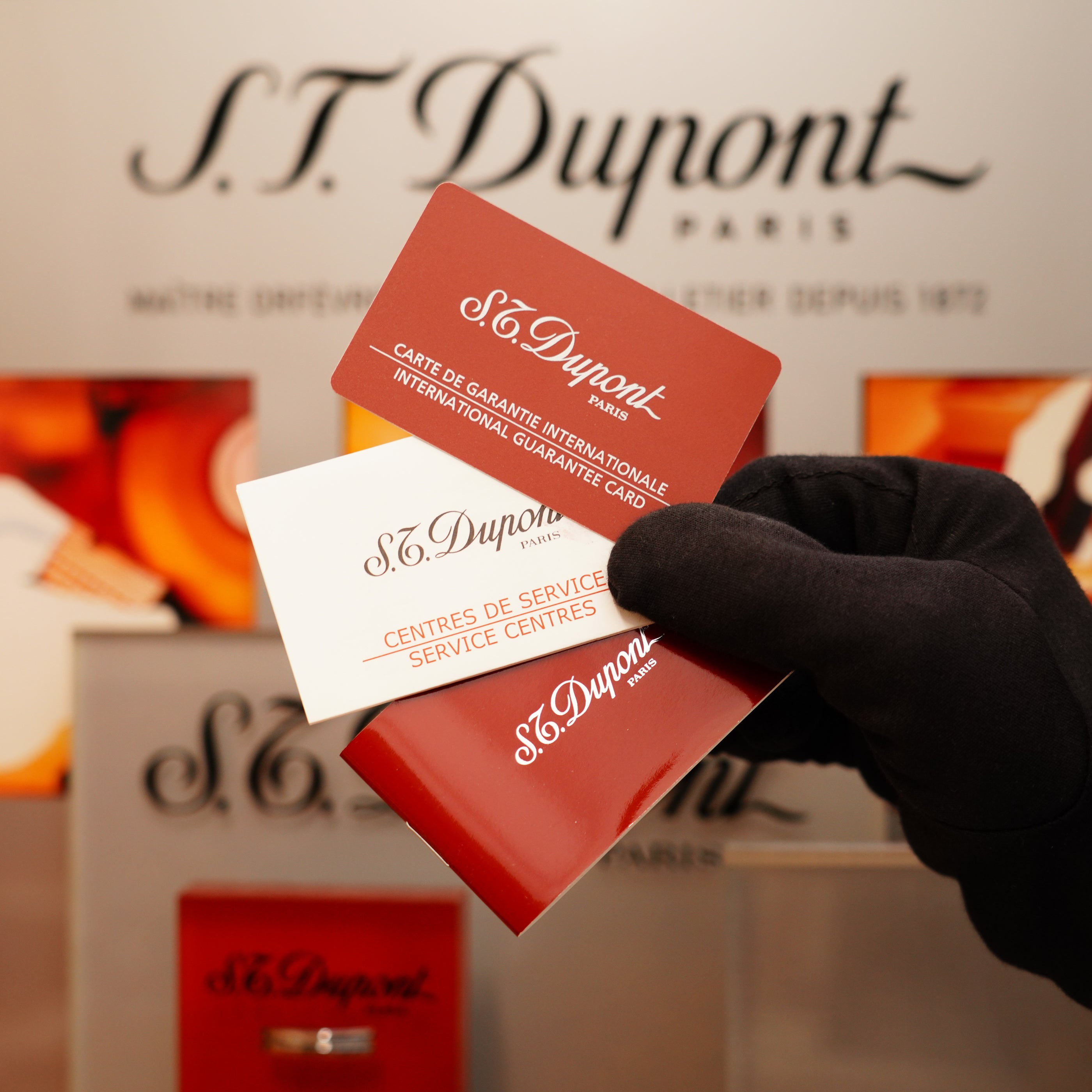 A gloved hand holds a guarantee and service center card from S.T. Dupont's Vintage 2000 Heavy Silver Finish Small iconic Ligne 1 Vertical Ligne Lighter in front of an S.T. Dupont display.