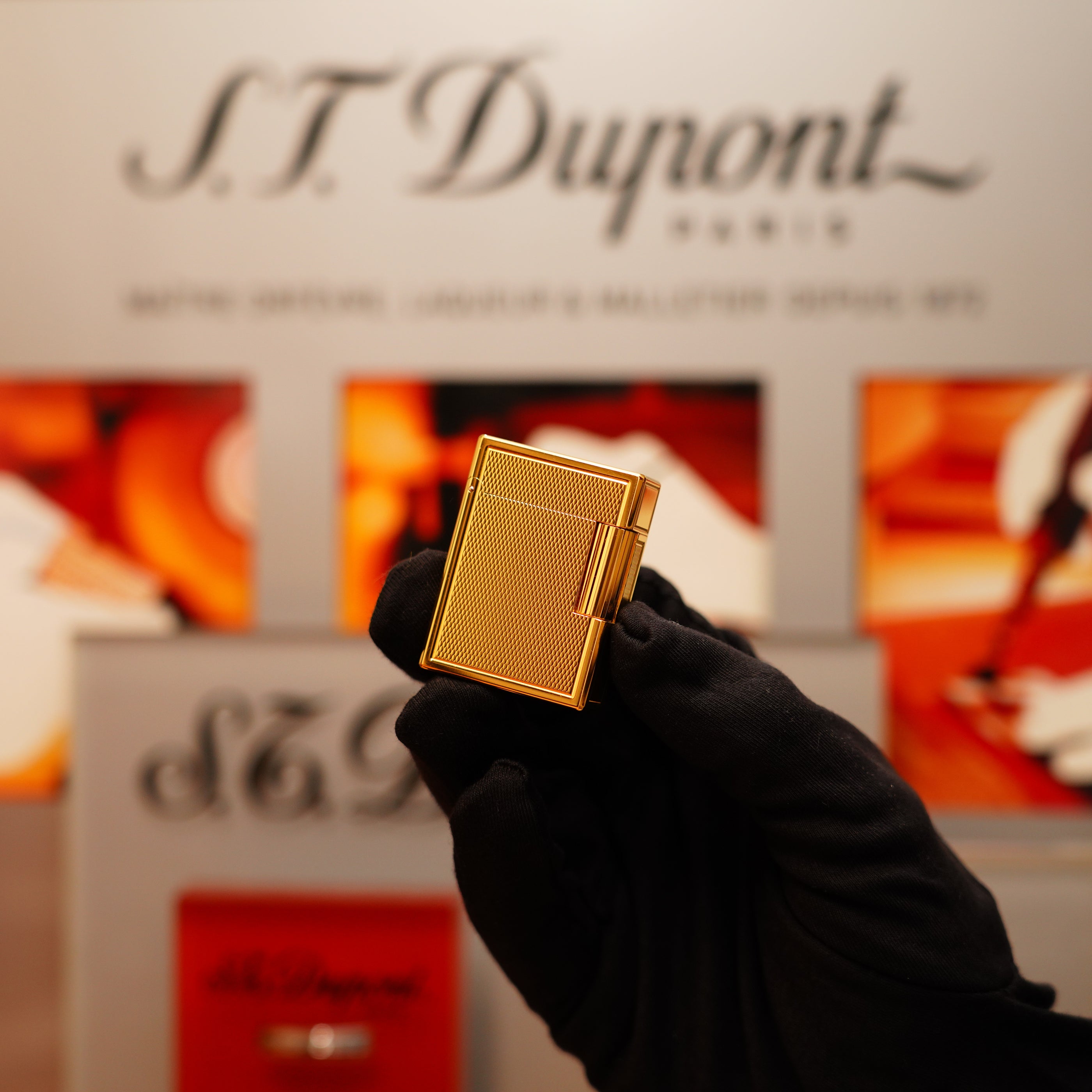 A gloved hand holds a Vintage 1996 S.T. Dupont 24k Small Grain d'Org Iconic Ligne 1 lighter with a textured surface, set against a blurred background.