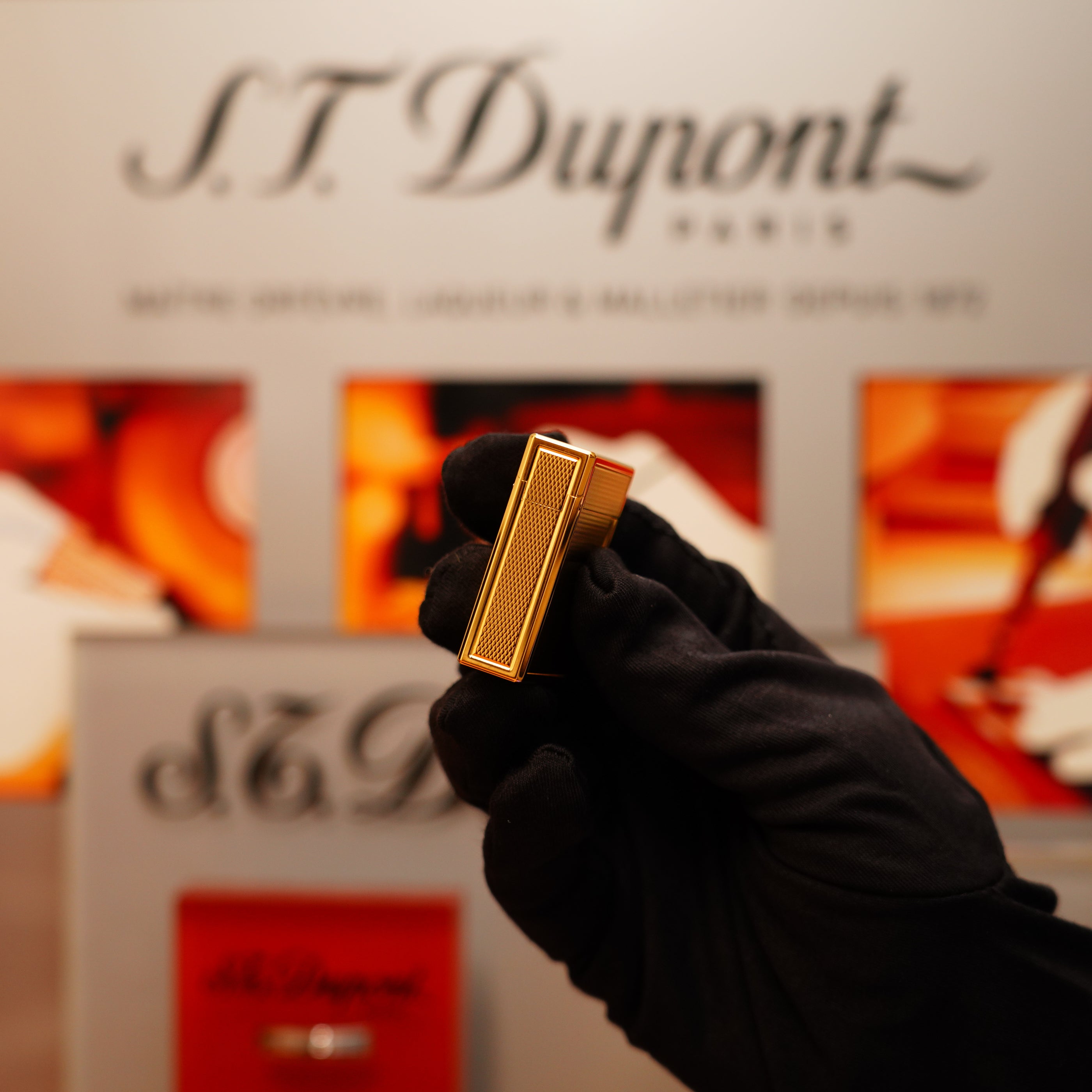 A gloved hand holds a Vintage 1996 St Dupont 24k Small Grain d'Org Iconic Ligne 1 Heavy Finish Lighter in front of a branded display backdrop.