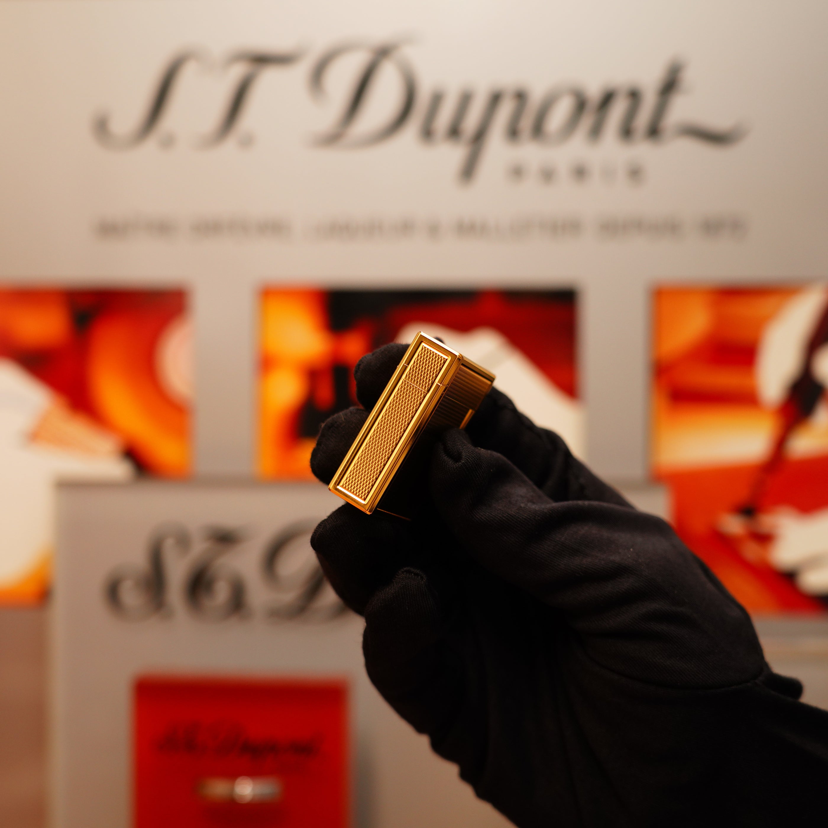 A gloved hand holds a gold Vintage 1996 S.T. Dupont 24k Small Grain d'Org Iconic Ligne 1 Heavy Finish Lighter against a blurred background with the S.T. Dupont logo.