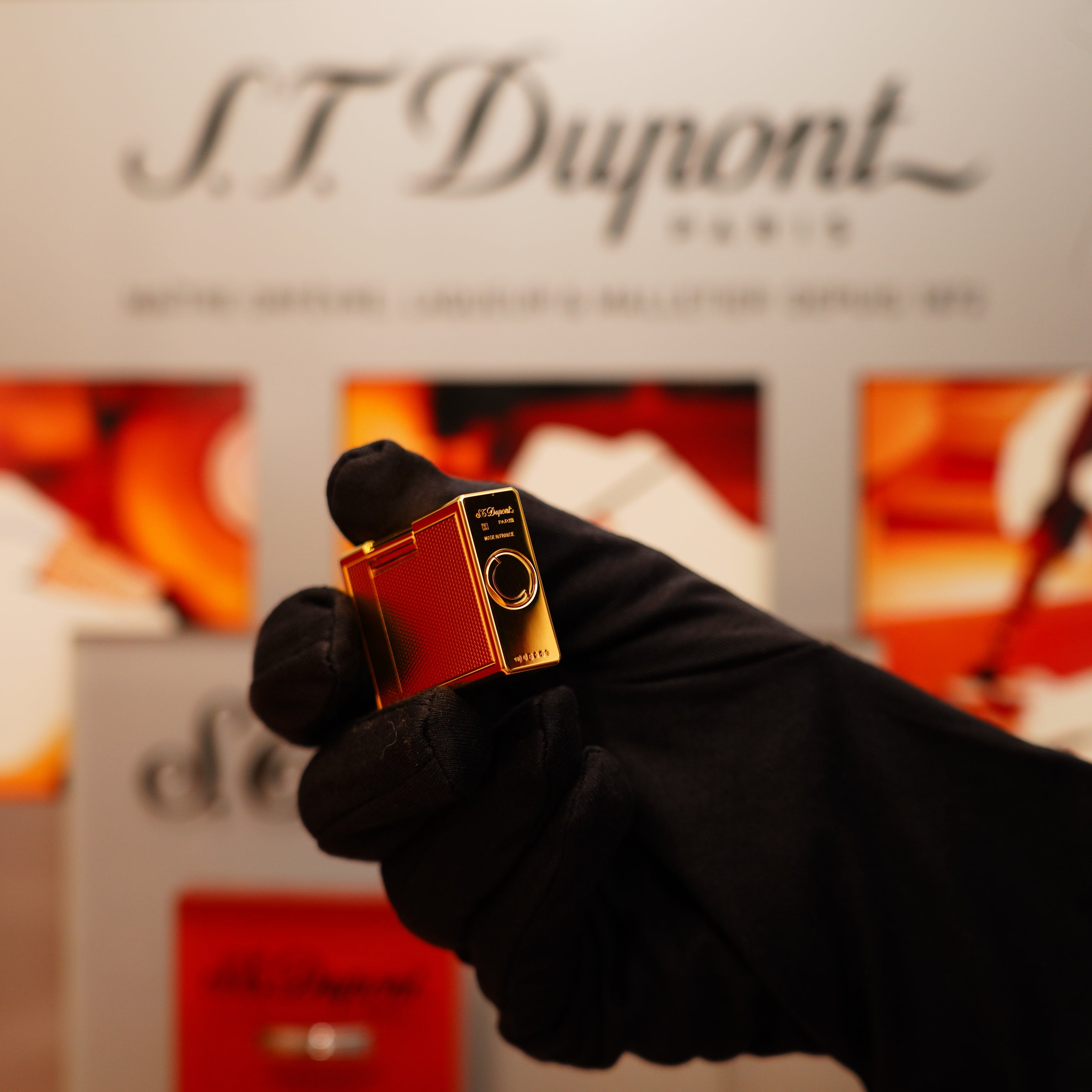 A gloved hand holds a small, red Vintage 1996 S.T. Dupont Ligne 1 lighter against a blurred branded backdrop.