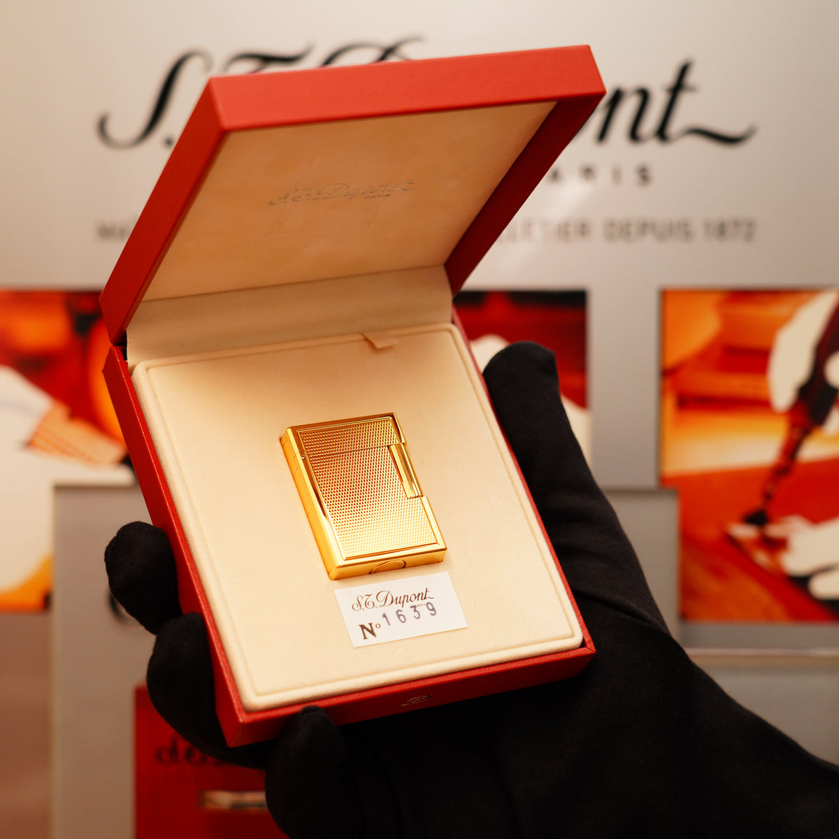 A hand in a black glove holds an open red box displaying a gold S.T. Dupont lighter labeled "Vintage 1996 St Dupont 24k Small Grain d'Org Iconic Ligne 1 Heavy Finish Lighter.