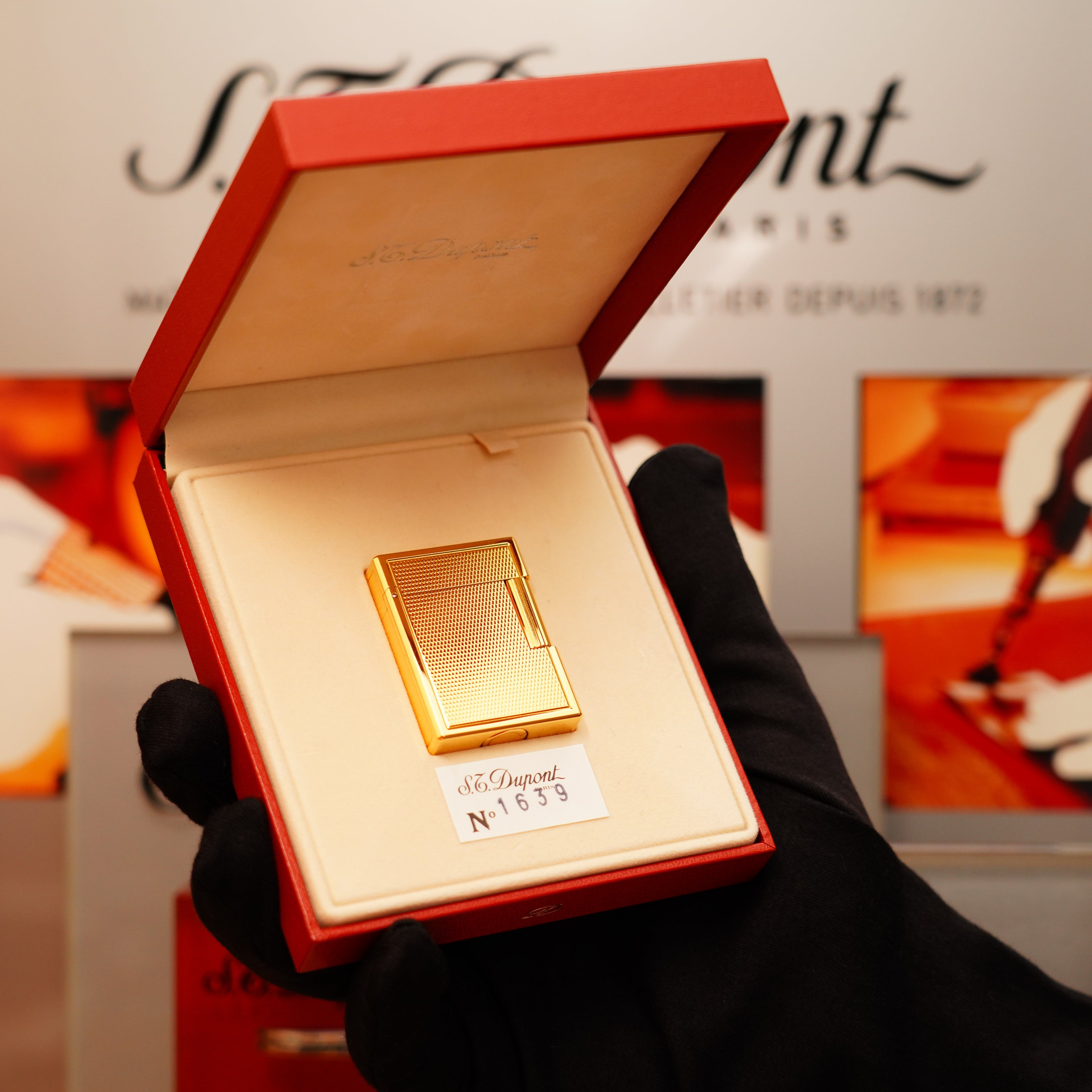 A hand in a black glove holds an open red box displaying a gold S.T. Dupont lighter labeled "Vintage 1996 St Dupont 24k Small Grain d'Org Iconic Ligne 1 Heavy Finish Lighter.