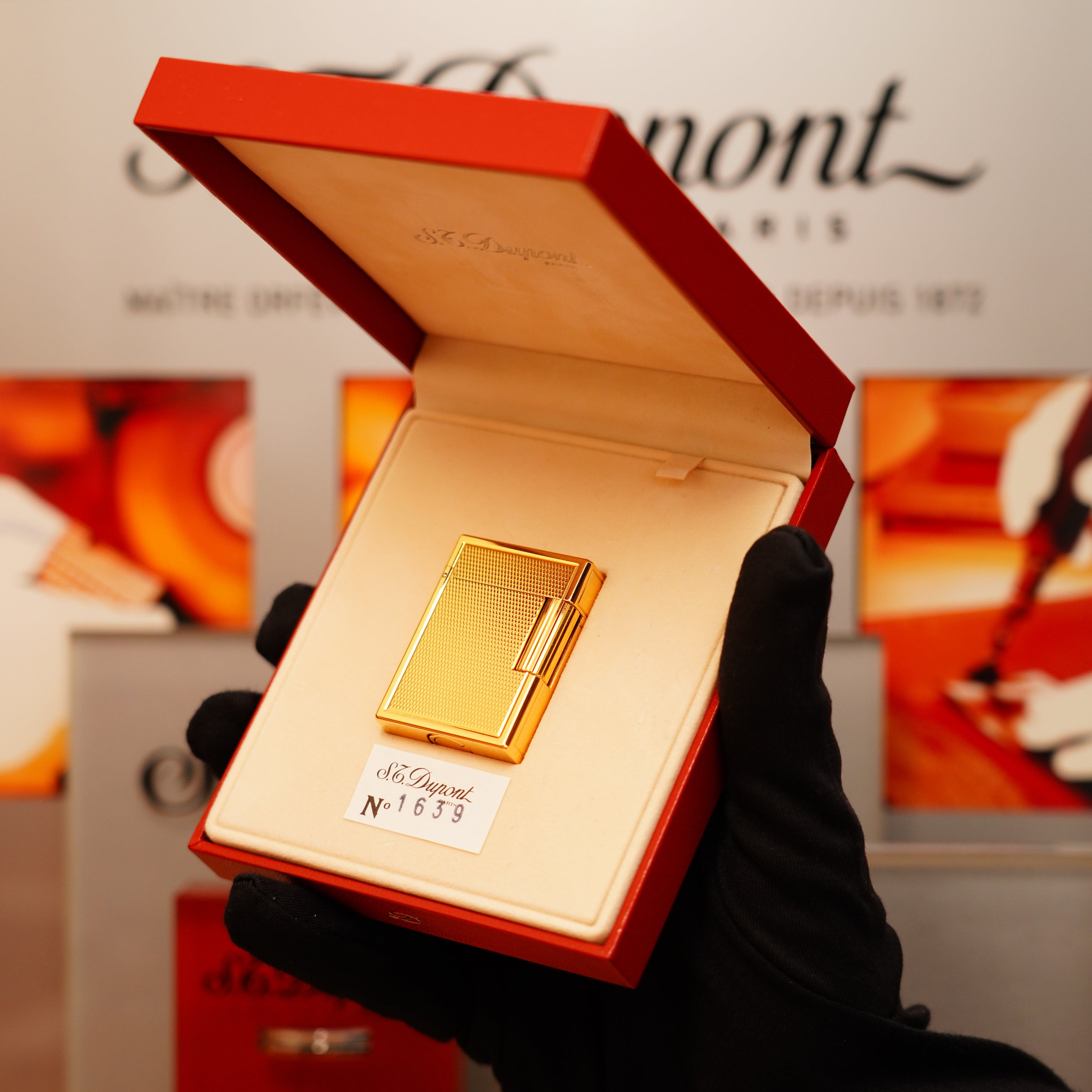 A gloved hand holds an open red box adorned with "S.T. Dupont Paris," containing a Vintage 1996 St Dupont 24k Small Grain d'Org Iconic Ligne 1 Heavy Finish Lighter, labeled "N°1653.