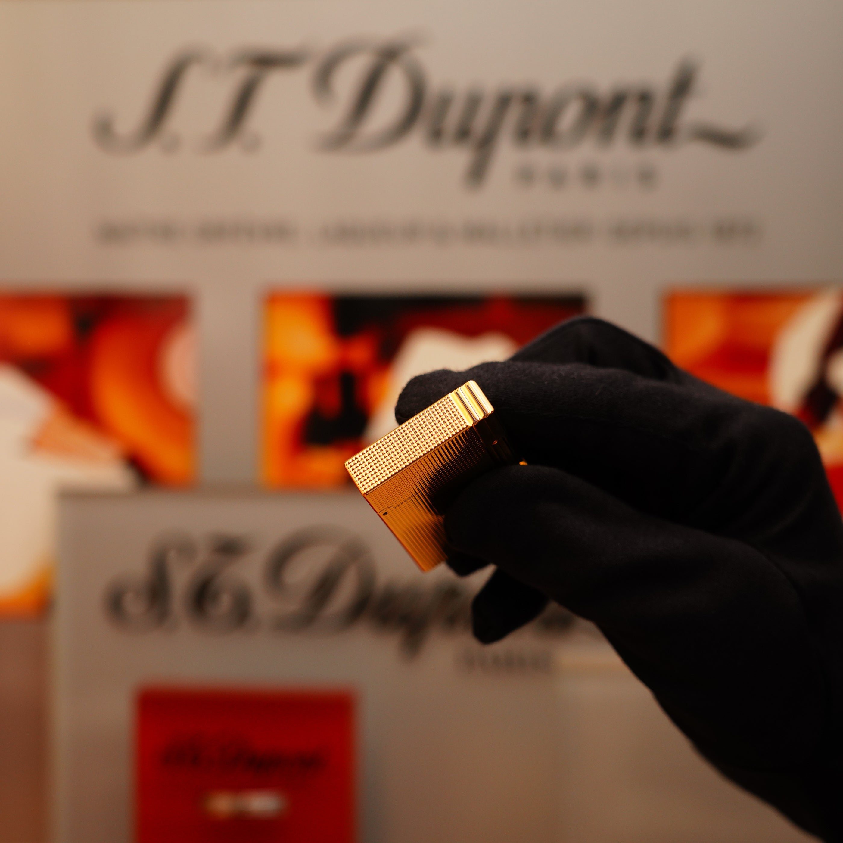 A gloved hand holds the Vintage 2002 S.T. Dupont Ligne 2 lighter in heavy 24k gold finish, showcasing its Gatsby vertical line pattern against an S.T. Dupont backdrop.