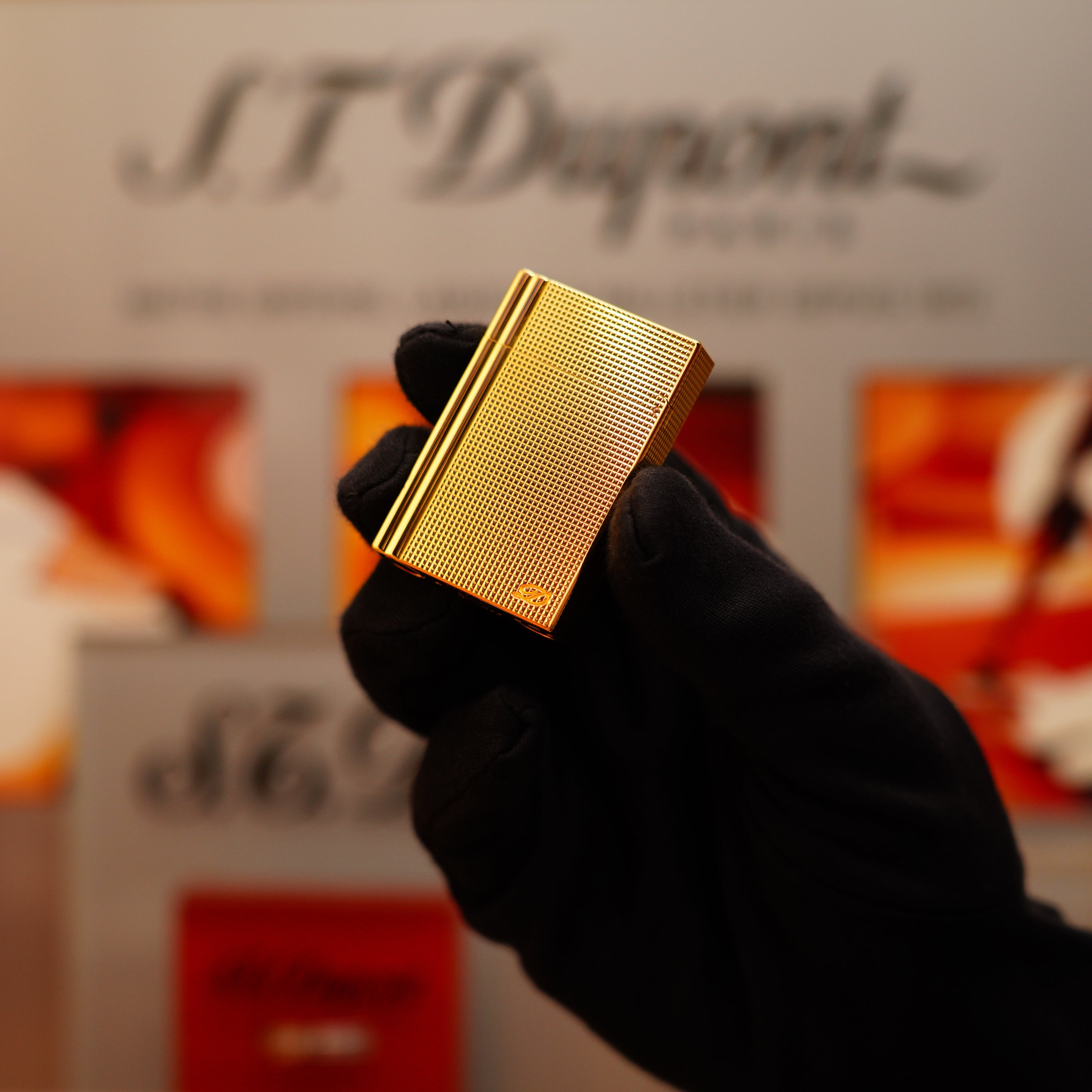 A gloved hand holds a Vintage 2002 St Dupont Rare Heavy 24k Gold Finish Gatsby Vertical Line Pattern Ligne 2 Lighter against a blurred background featuring the S.T. Dupont logo.