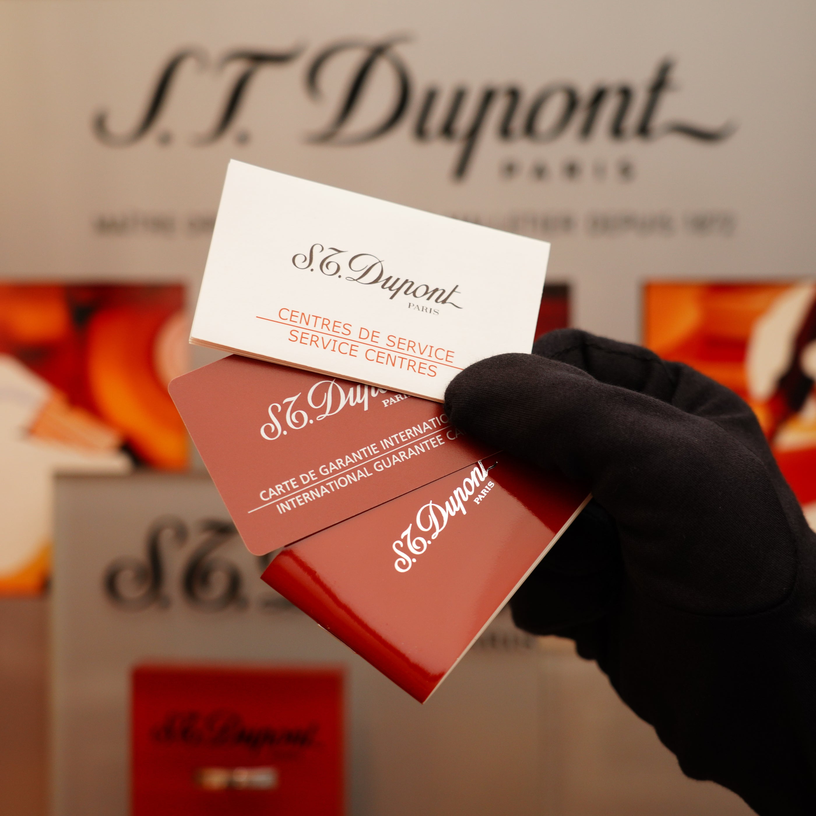A gloved hand showcases two S.T. Dupont service and guarantee cards with a blurred backdrop, highlighting the Vintage 2002 St Dupont Rare Heavy 24k Gold Finish Gatsby Vertical Line Pattern Ligne 2 Lighter.