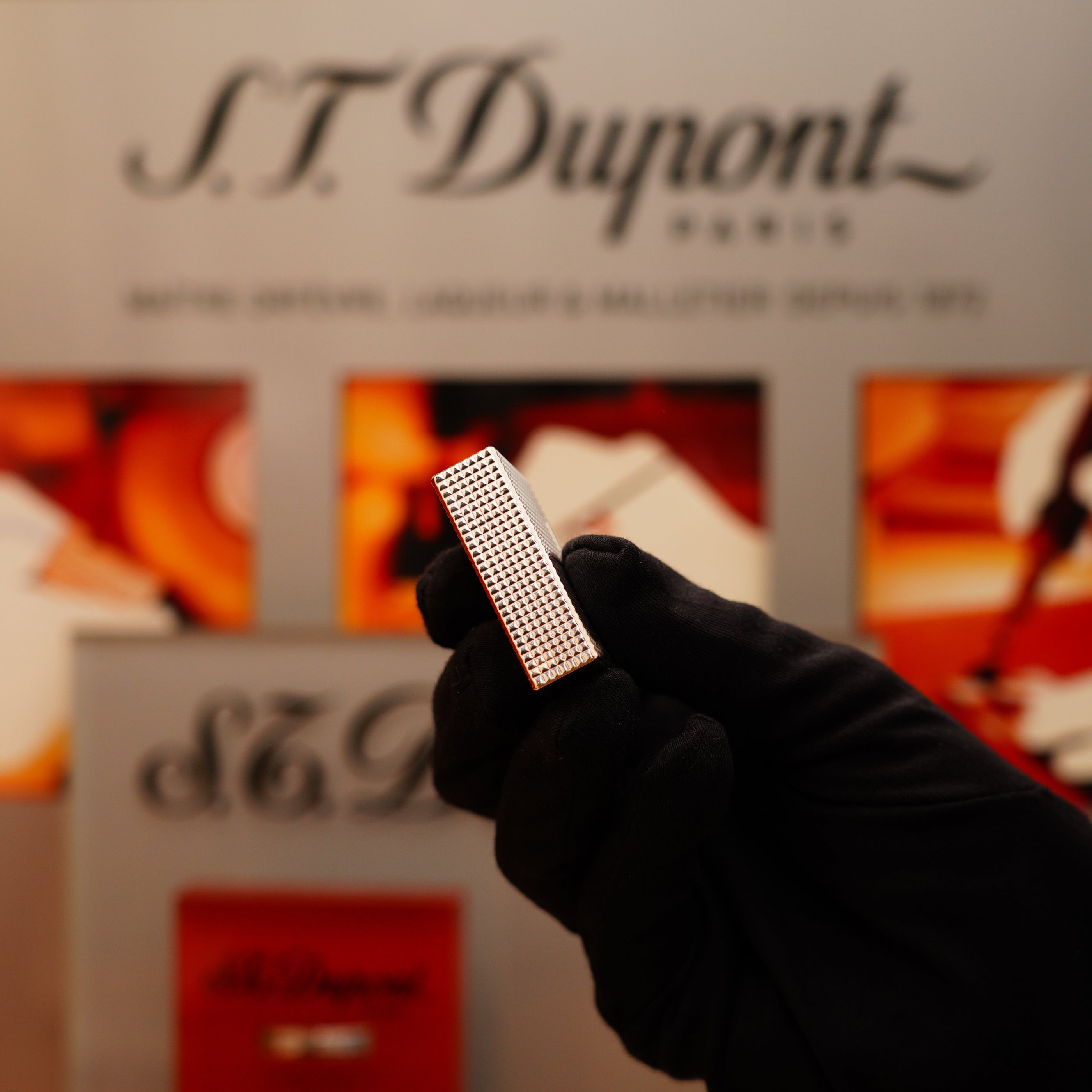 A gloved hand holds a Vintage 1996 S.T. Dupont Ligne 1 Diamond Head Pattern small heavy silver finish lighter in front of a branded display.