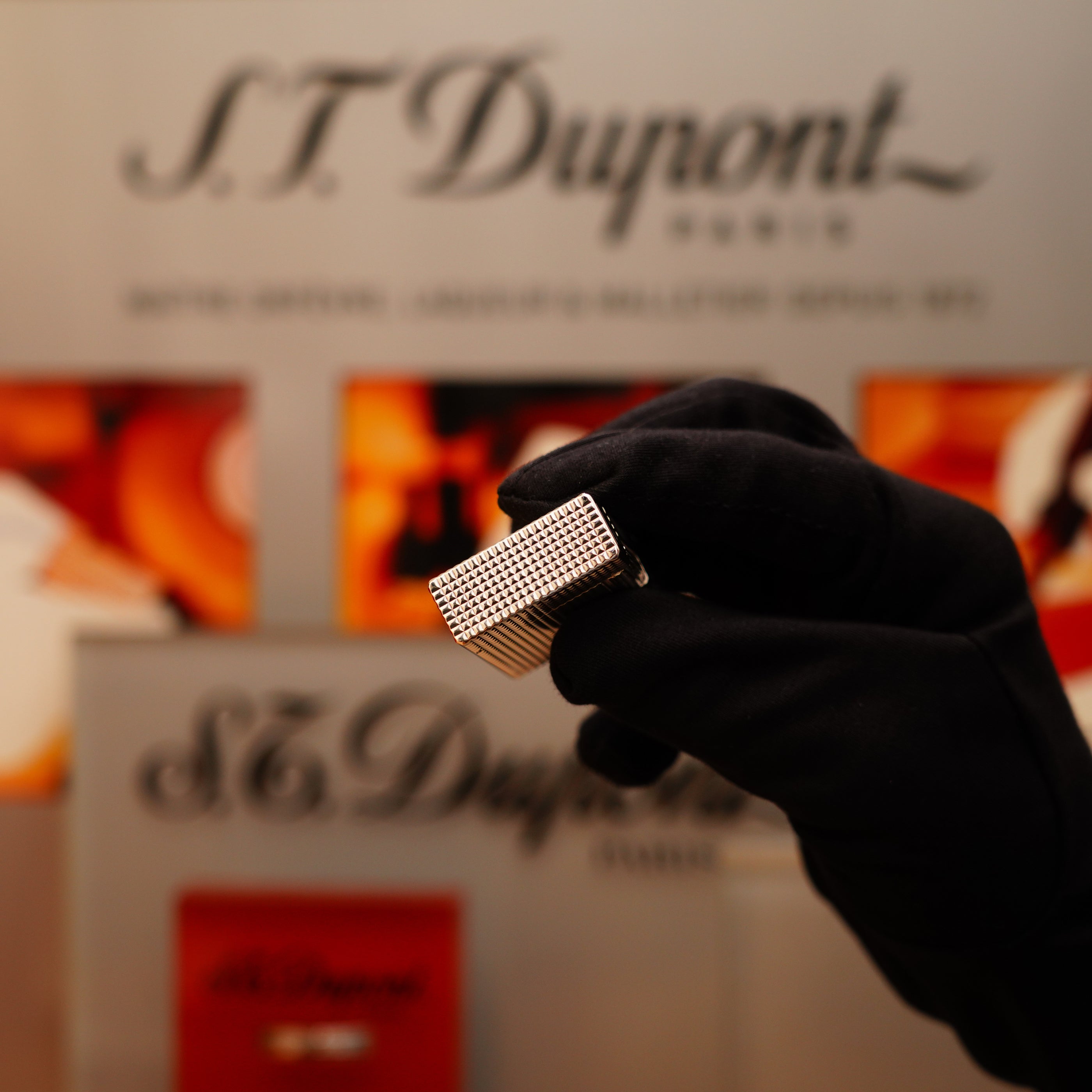 A gloved hand holds a Vintage 1996 S.T. Dupont Ligne 1 lighter with a Diamond Head Pattern in heavy silver finish, set against a blurred S.T. Dupont Paris sign.