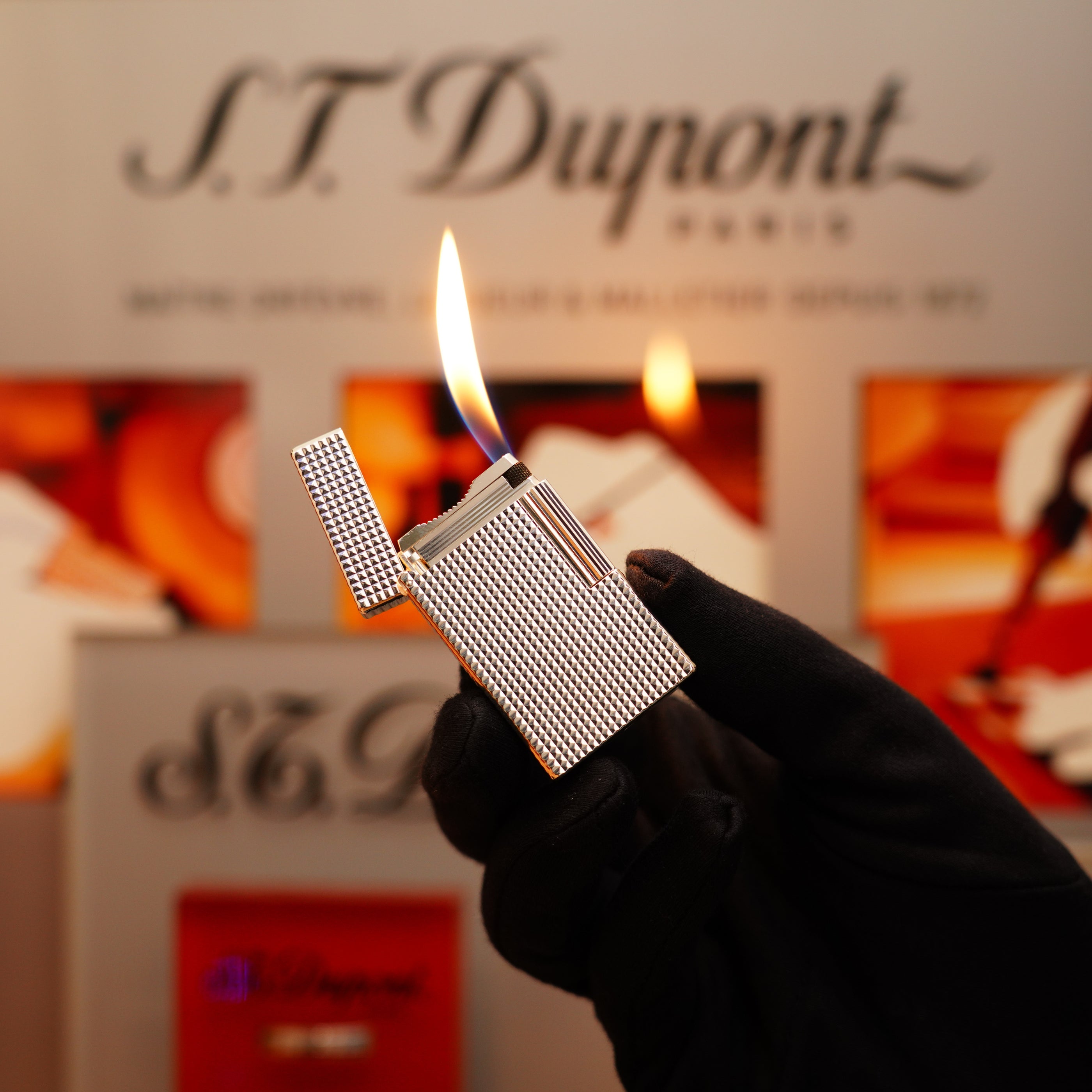 A gloved hand holds an open Vintage 1996 S.T. Dupont Ligne 1 Diamond Head Pattern Large Heavy Silver Finish Lighter, showcasing its lit flame against a blurred background displaying "S.T. Dupont Paris.