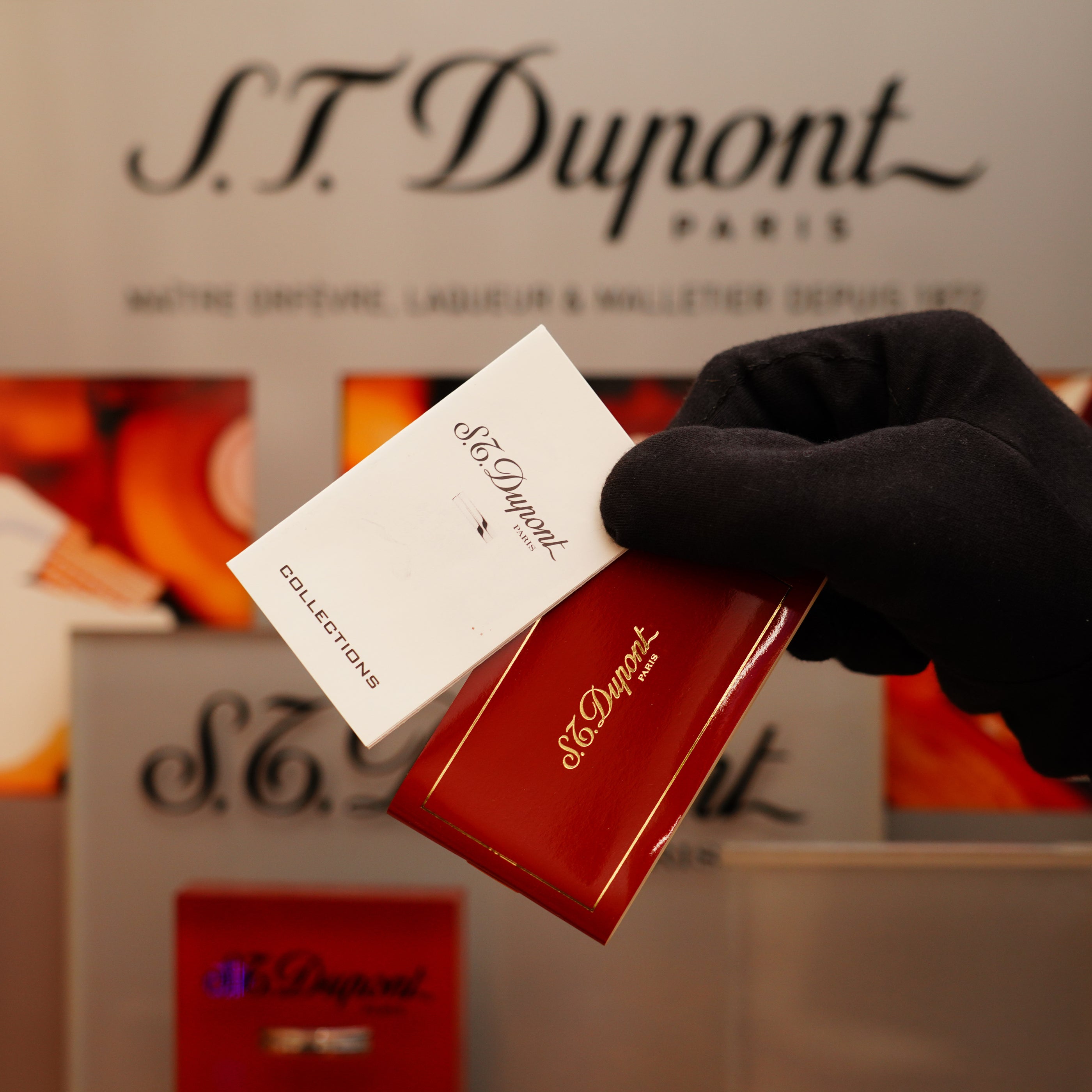 A gloved hand holds a Vintage 1996 St Dupont Ligne 1 Large Heavy Silver Finish Lighter gift card and red box, with the S.T. Dupont logo visible in the background.