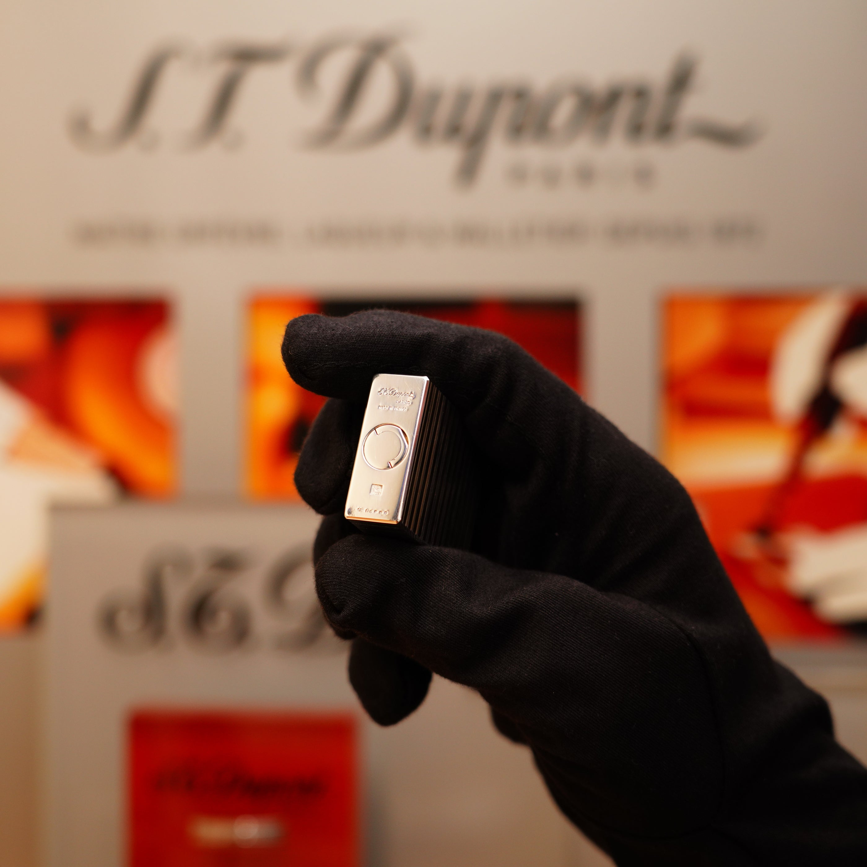 A gloved hand holding a Vintage 1996 St Dupont Ligne 1 small Horizontal line heavy silver finish lighter against a blurred background with the S.T. Dupont logo.