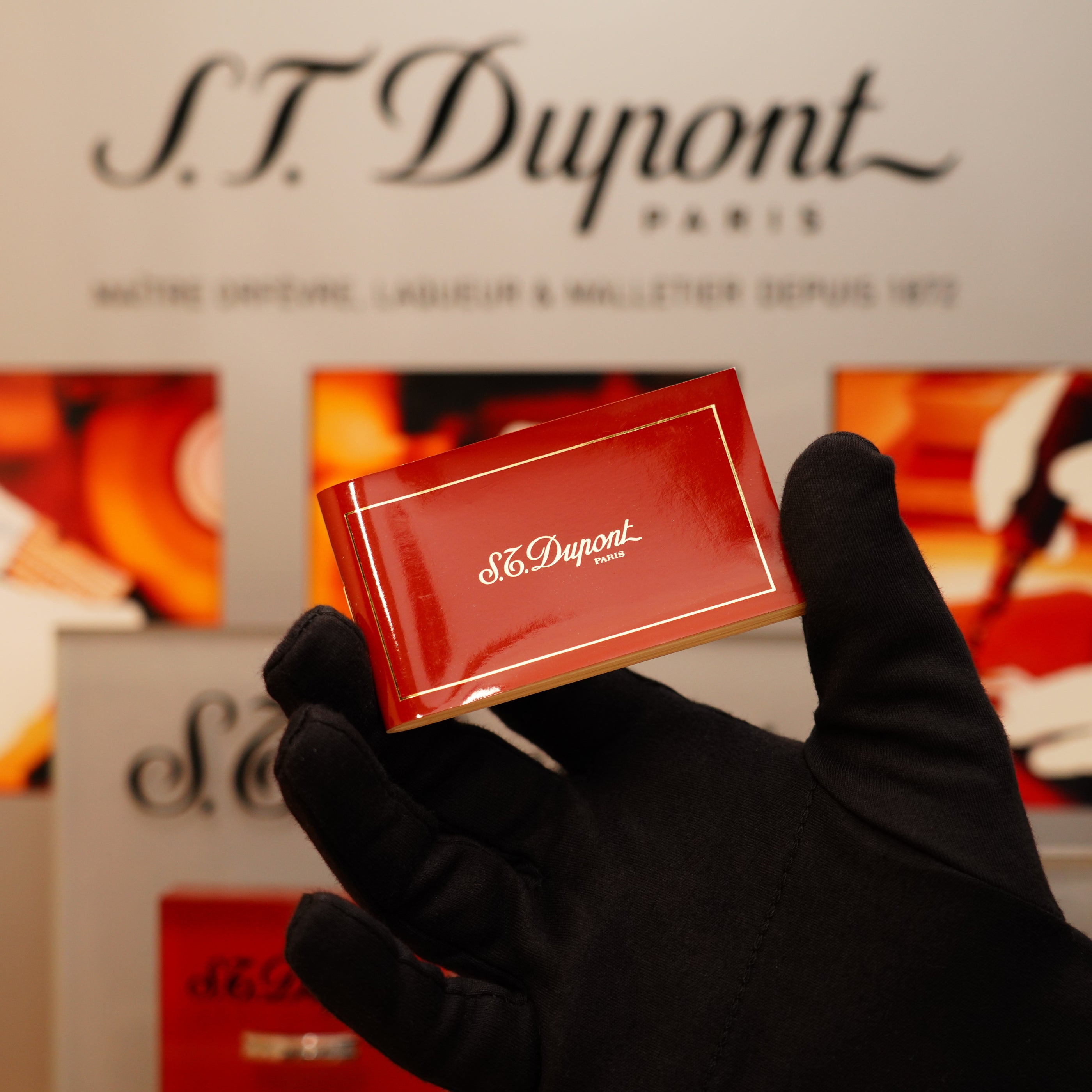 A gloved hand holding a S.T. Dupont Vintage 1996 Ligne 1 small Horizontal Line Heavy Silver Finish lighter in front of a blurred S.T. Dupont Paris display.