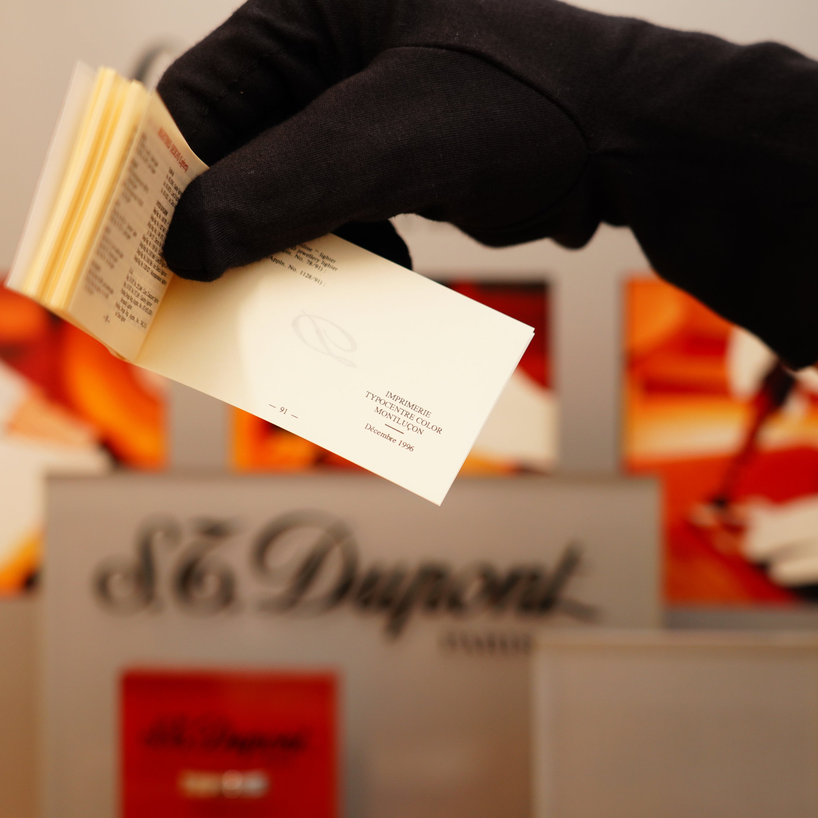 A hand in a black glove flips through business cards, set against a blurred background, featuring the S.T. Dupont brand known for its 1996 Ligne 1 Rare Heavy Silver Finish Vertical Line Pattern Lighter.