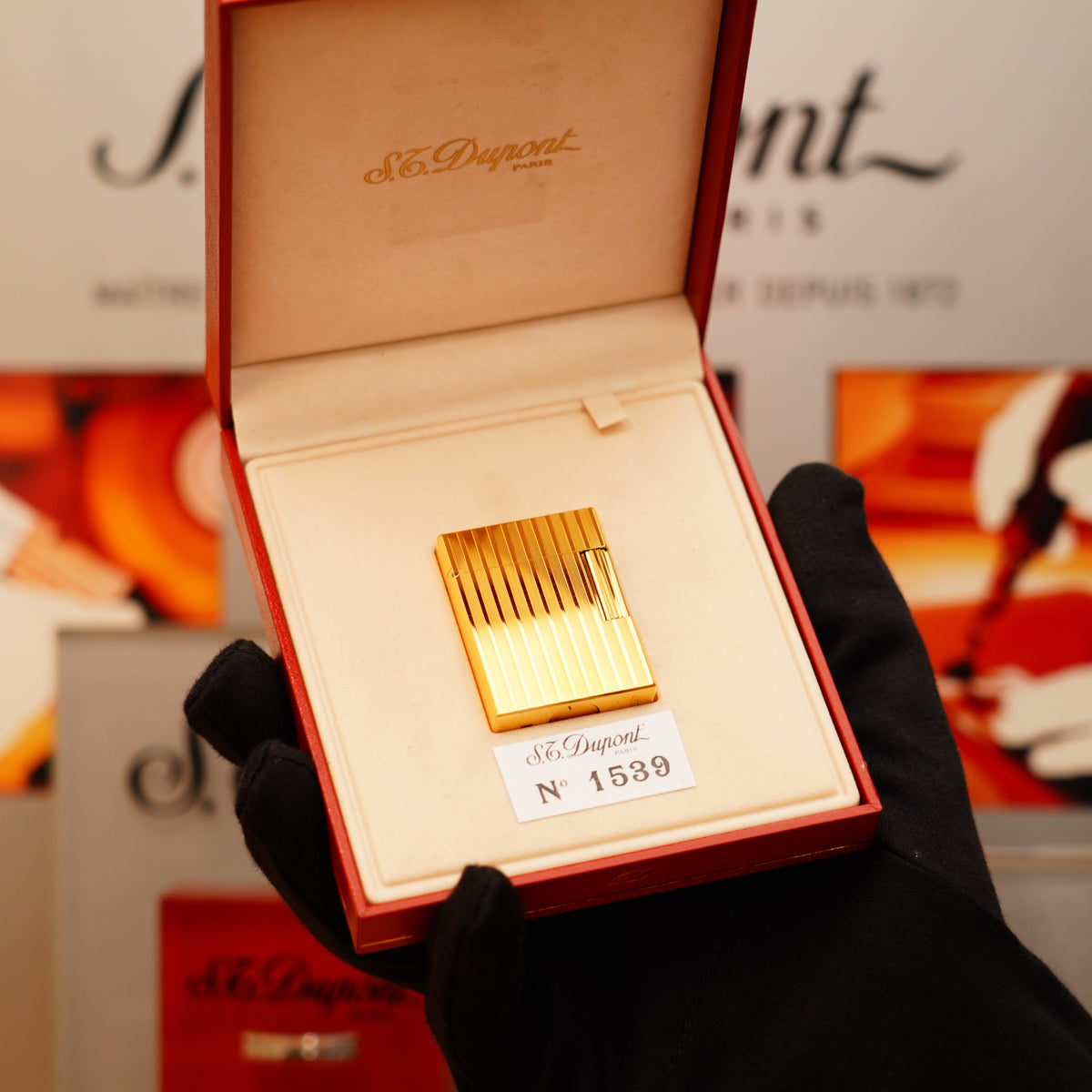 A gloved hand holds an open box showcasing a Vintage 1990 S.T. Dupont small Ligne 1 lighter with rare pattern and "1539," finished in 24k gold.