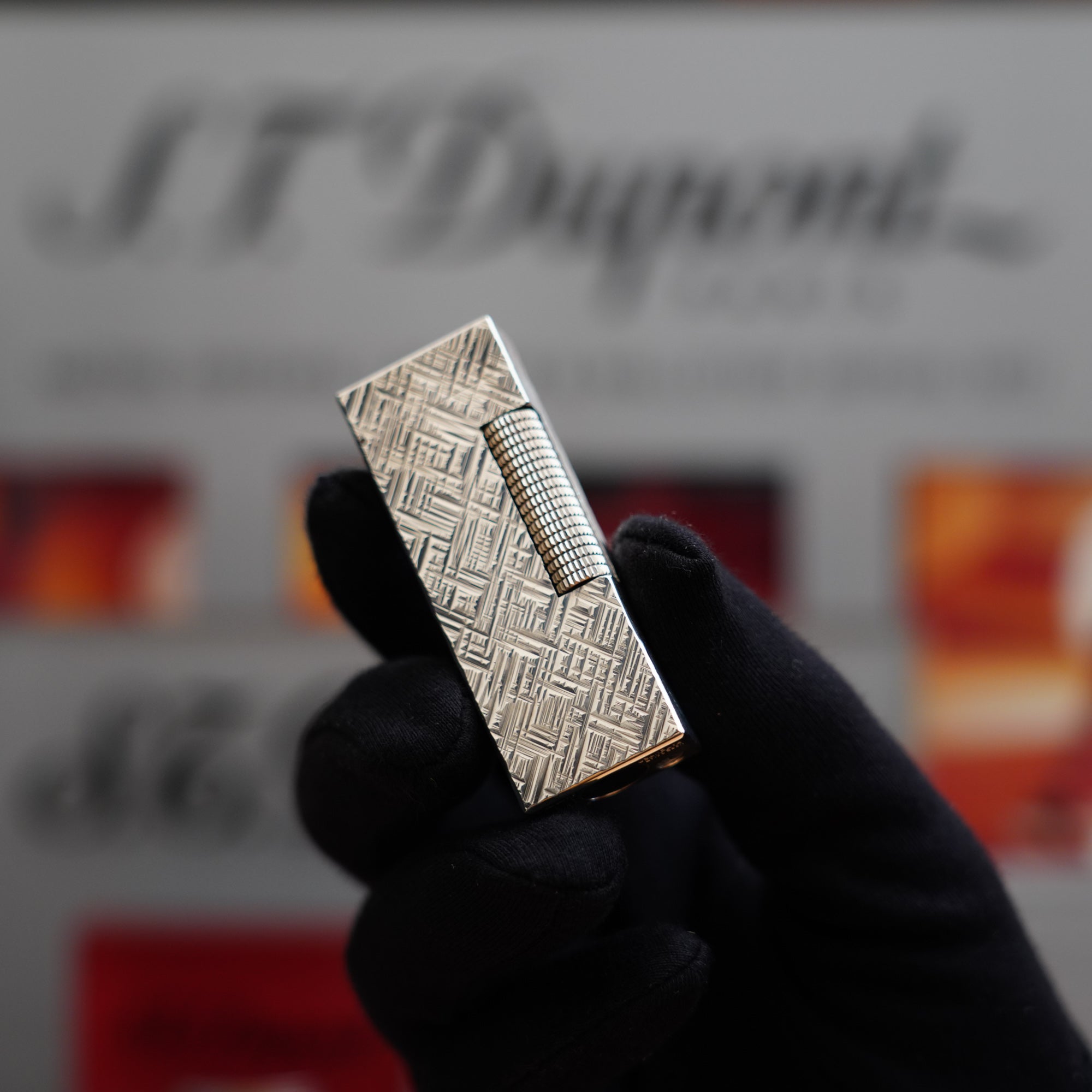 A vintage Dunhill Rollagas Silver Plated Florentine Pattern Lighter collector's item on display, with a hand holding it in front of a box.