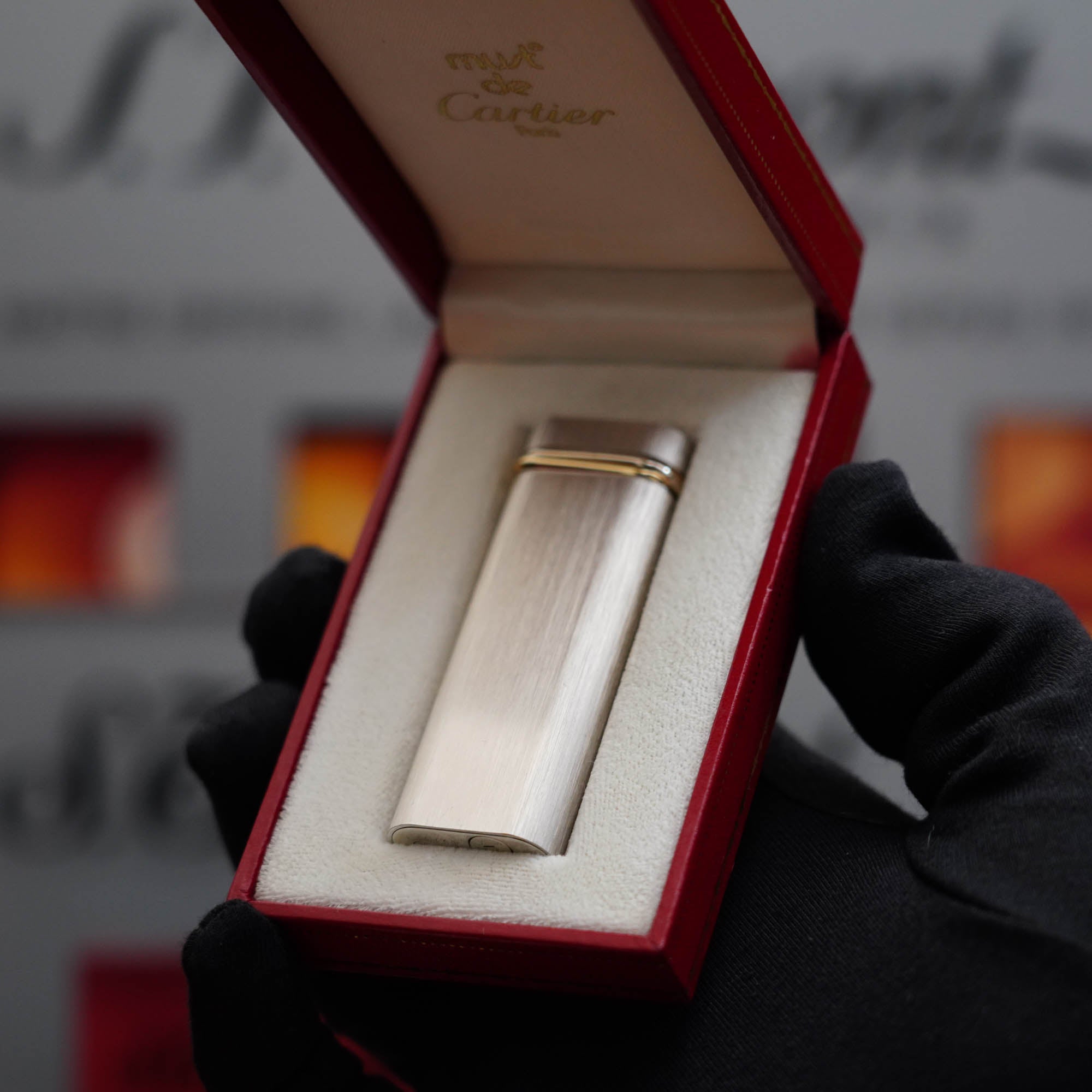 A person is holding a Vintage 1980 Cartier Palladium Plated 18k Trinity ring Lighter in a box.