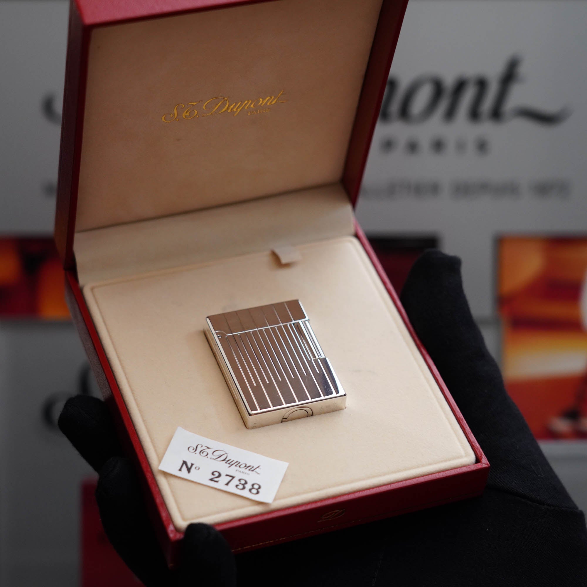 A person is holding a vintage 1980 S.T. Dupont Heavy Palladium Plated Small Size Ligne 1 Lighter in a box.