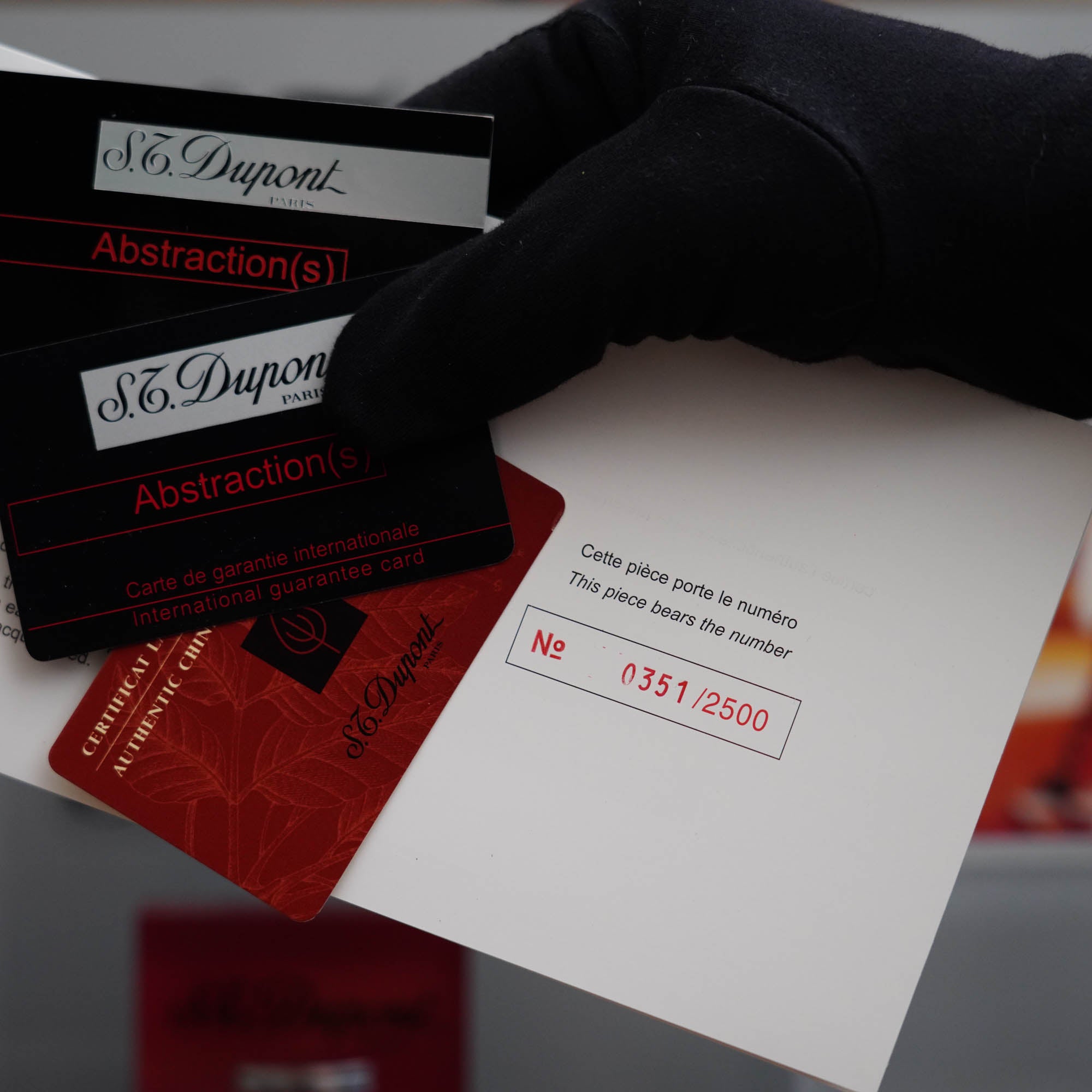 A person holding a Vintage 1990 Limited Heavy Palladium Finish S.T. Dupont Ligne 2 Abstraction Red Laquer Lighter and a business card.