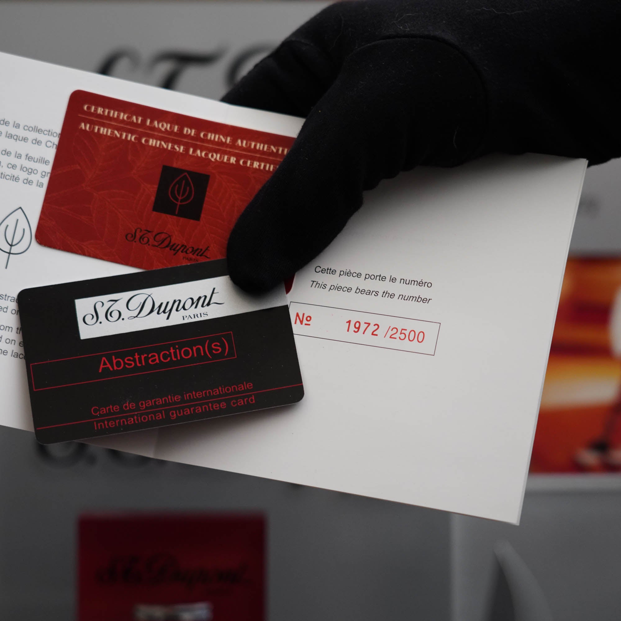 A person is holding a vintage 1990 limited heavy palladium finish St Dupont Ligne 2 Abstraction black laquer lighter collector's item card with a red envelope.