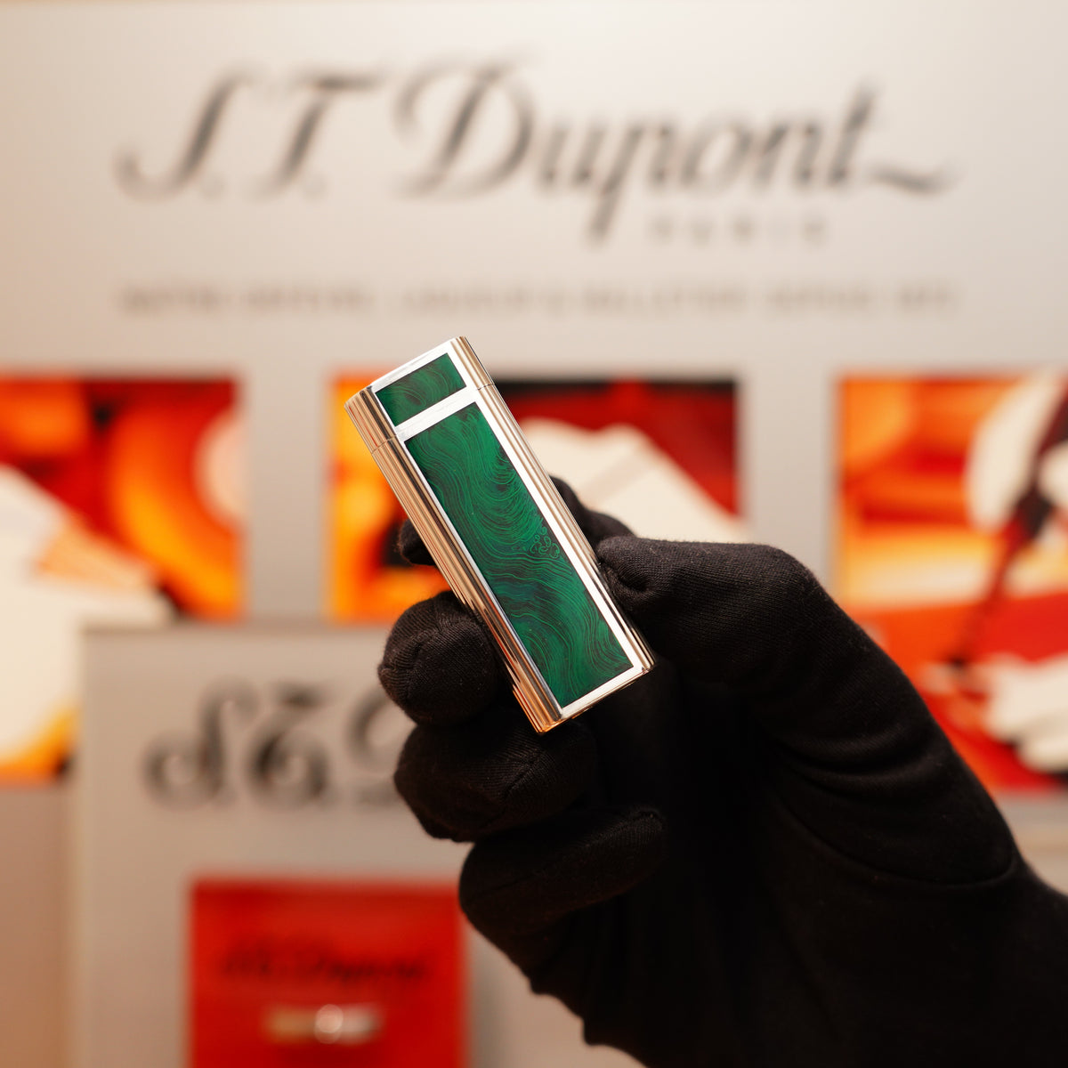 A gloved hand displays a Vintage 1970 Cartier Sterling Silver and Green Enamel lighter against a blurred background featuring the text "S.T. Dupont.