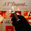 A gloved hand holding a lit Vintage 1970 Cartier solid 925 sterling silver natural half brown lacquer rare lighter against a blurred background with the Cartier logo.