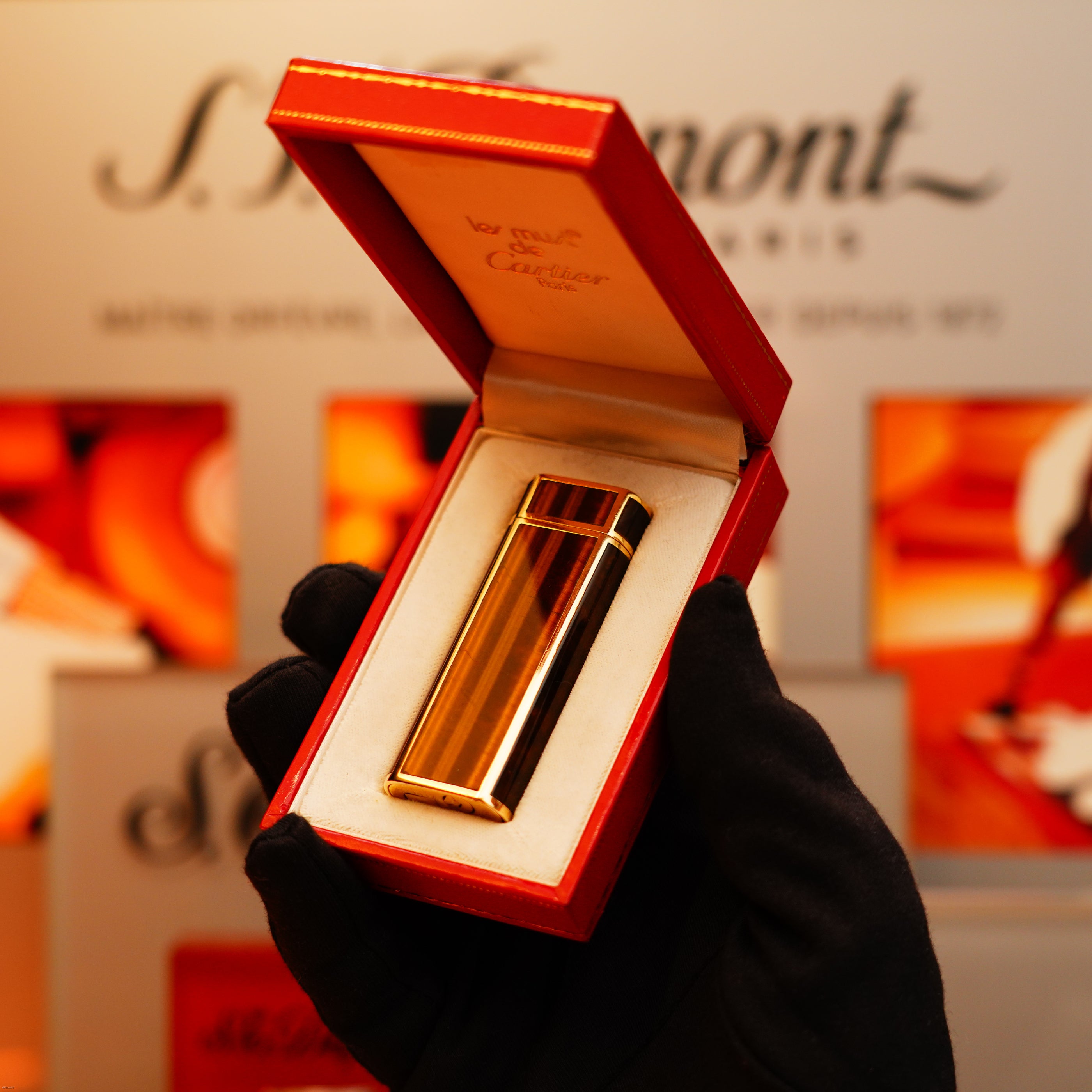 A gloved hand holds an open red box displaying a Vintage 1970 Cartier Extremely Rare Tiger's Eye Solid 18k Heavy Body with 750 hallmark Lighter from KirbyAllison.com, with the brand name visible in the background.