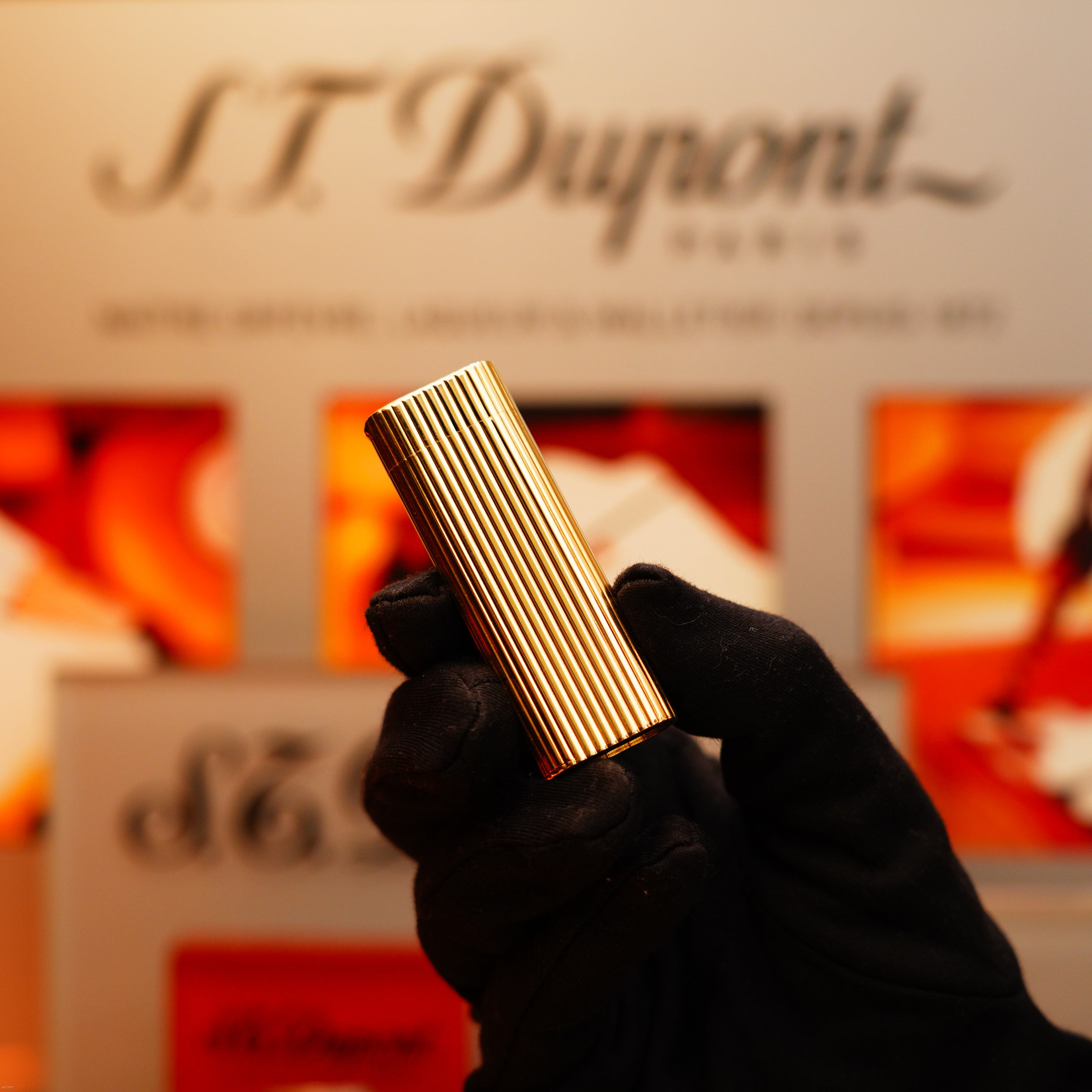 A gloved hand holds a Vintage 1970 Extremely Rare Cartier Solid 18k Gold Vertical Line Lighter with 750 hallmarks by KirbyAllison.com in front of a display background.