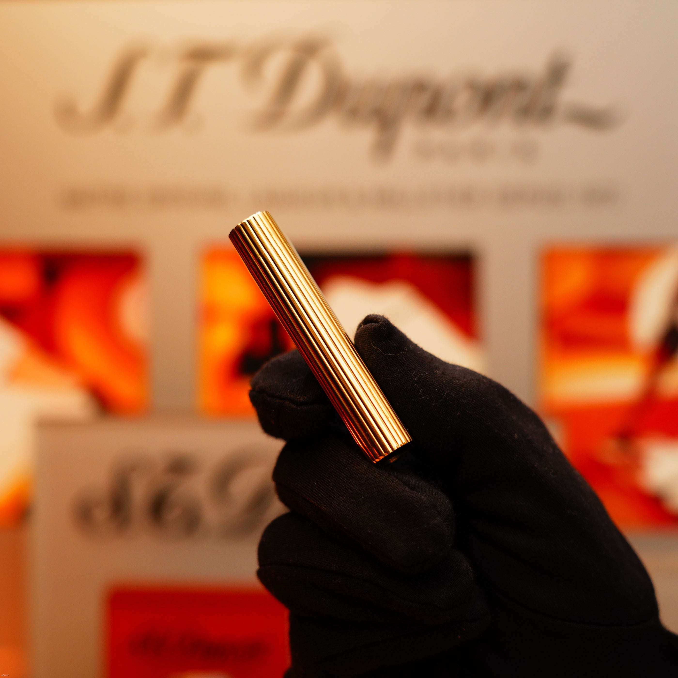 A gloved hand holds the Vintage 1970 Extremely Rare Cartier Solid 18k Gold Vertical Line Heavy Lighter with 750 hallmarks from KirbyAllison.com, set against a blurred background with red accents.