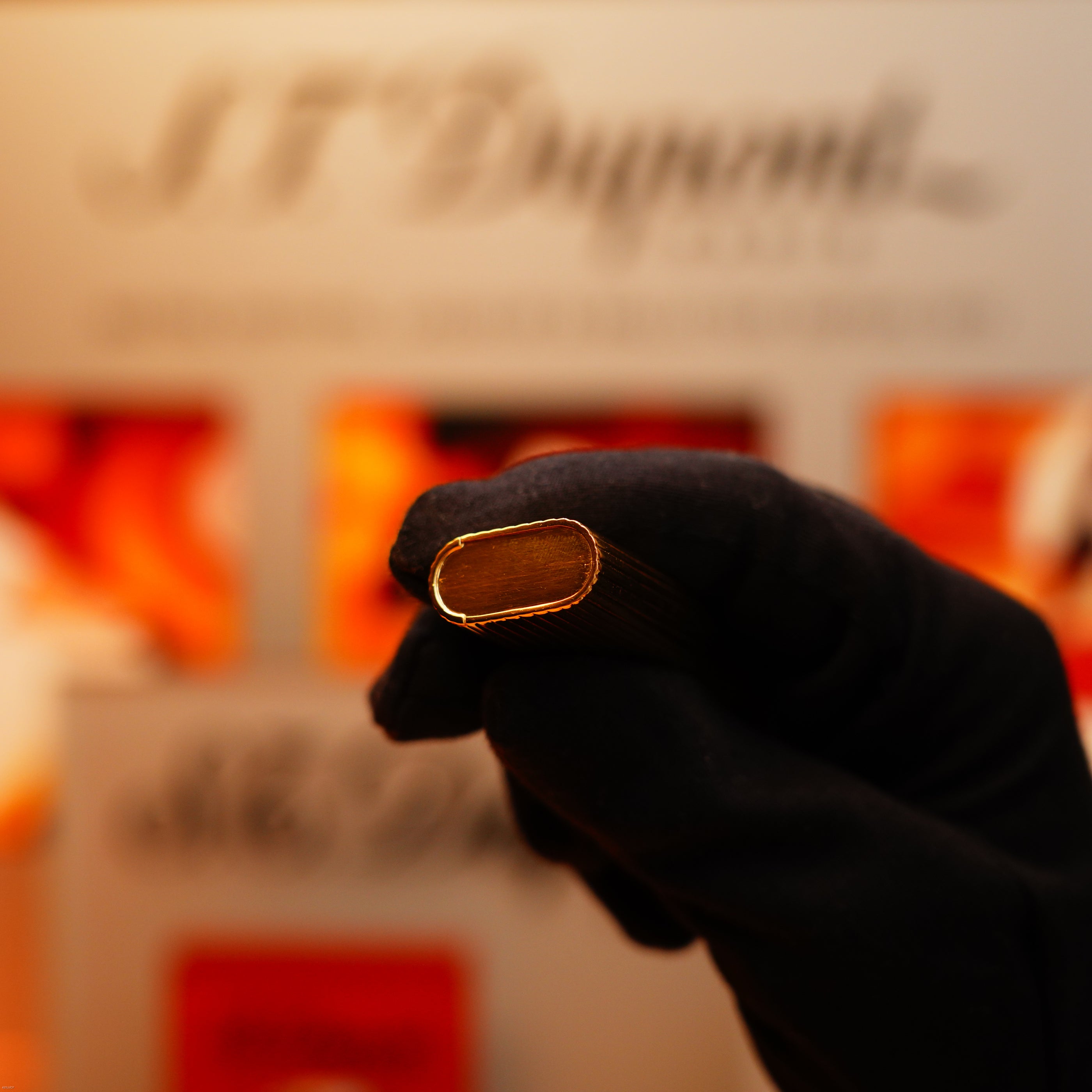 A gloved hand holds a Vintage 1970 Extremely Rare Cartier Solid 18k Gold Vertical Line Heavy Lighter with 750 hallmarks from KirbyAllison.com, with the text "ST Dupont" visible in the blurred background.