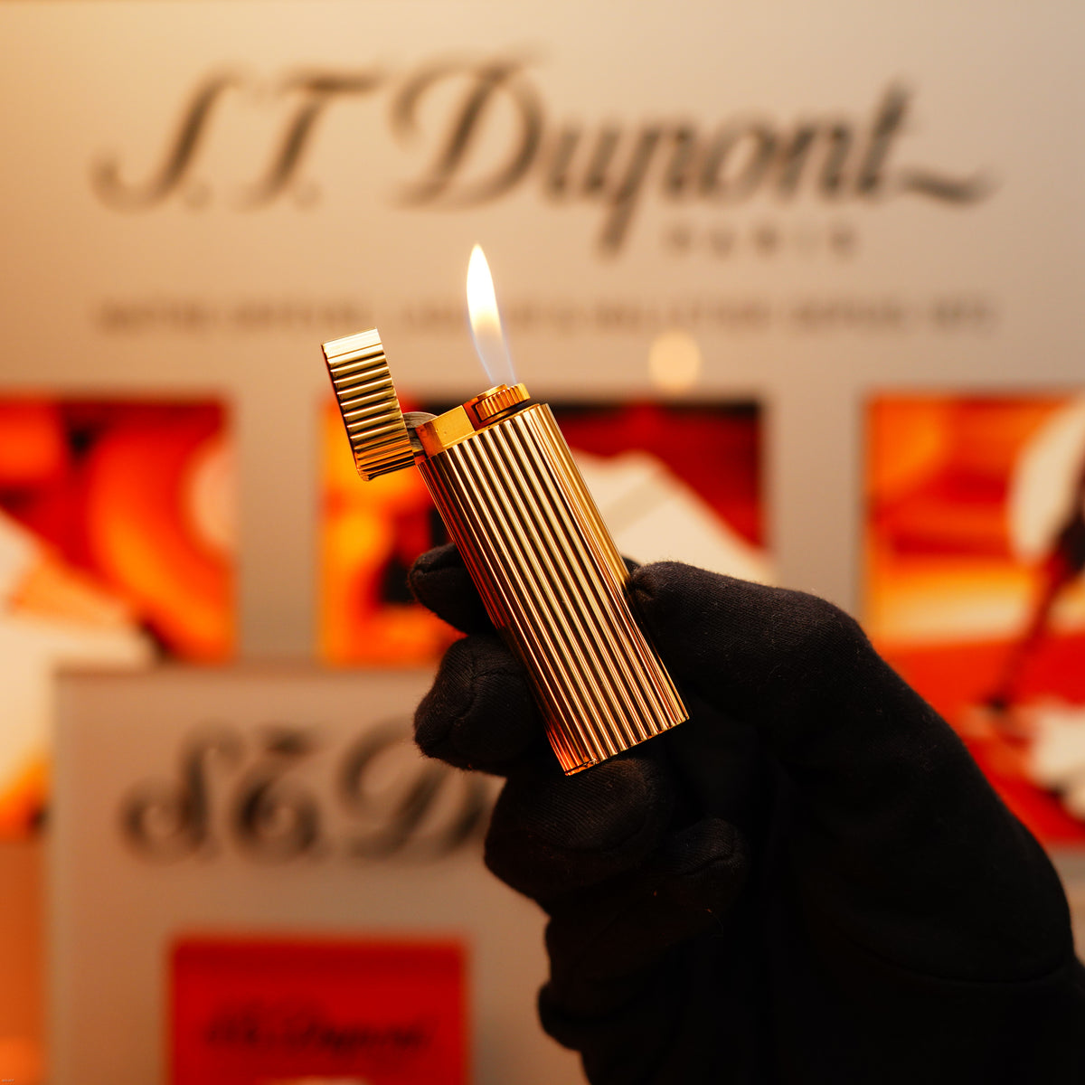 A gloved hand holds a Vintage 1970 Extremely Rare Cartier Solid 18k Gold Lighter from KirbyAllison.com, its flame lit, with a blurred sign in the background.