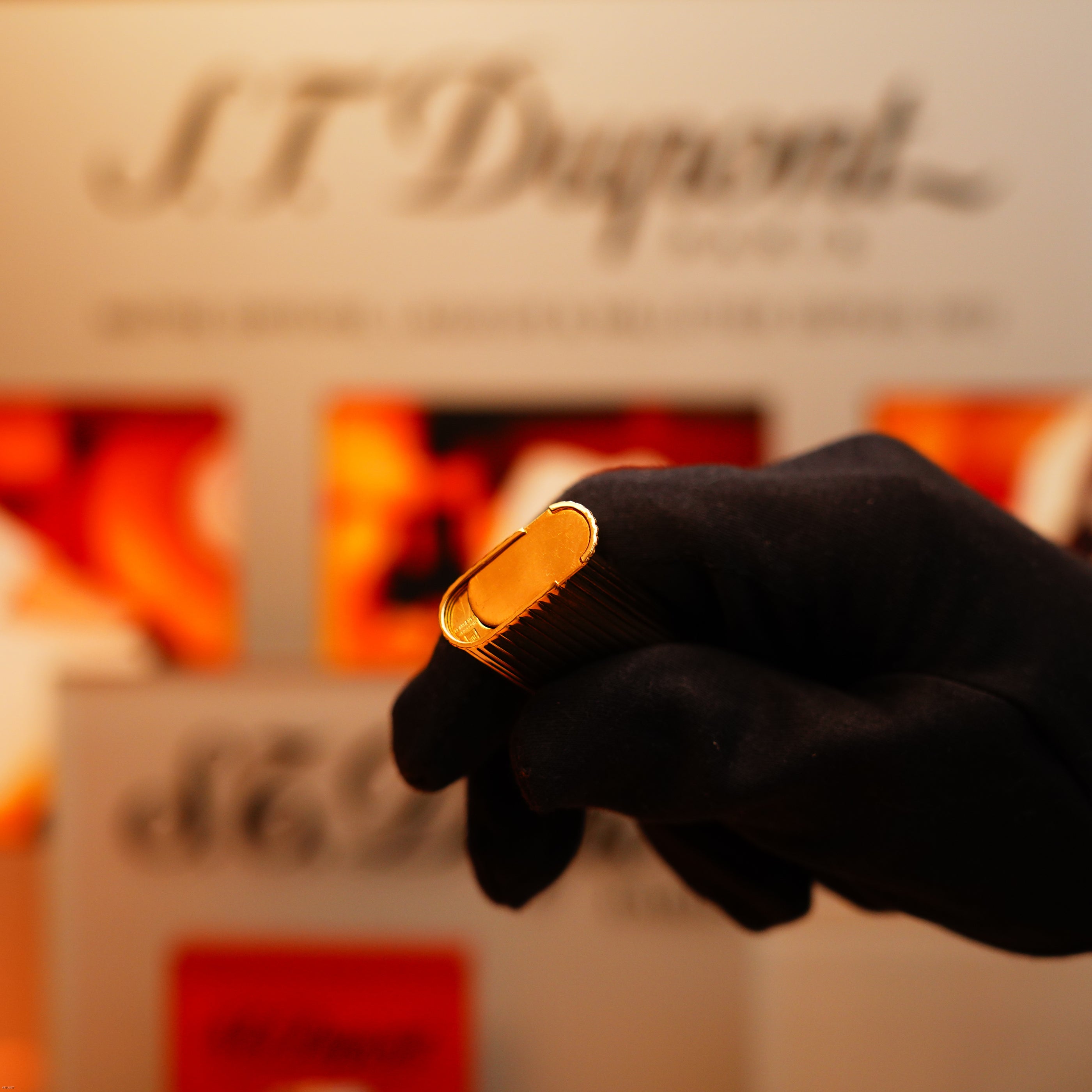 A gloved hand holds a Vintage 1970 Extremely Rare Cartier Solid 18k Gold Vertical Line Heavy Lighter with 750 hallmarks from KirbyAllison.com in front of a blurred display background.