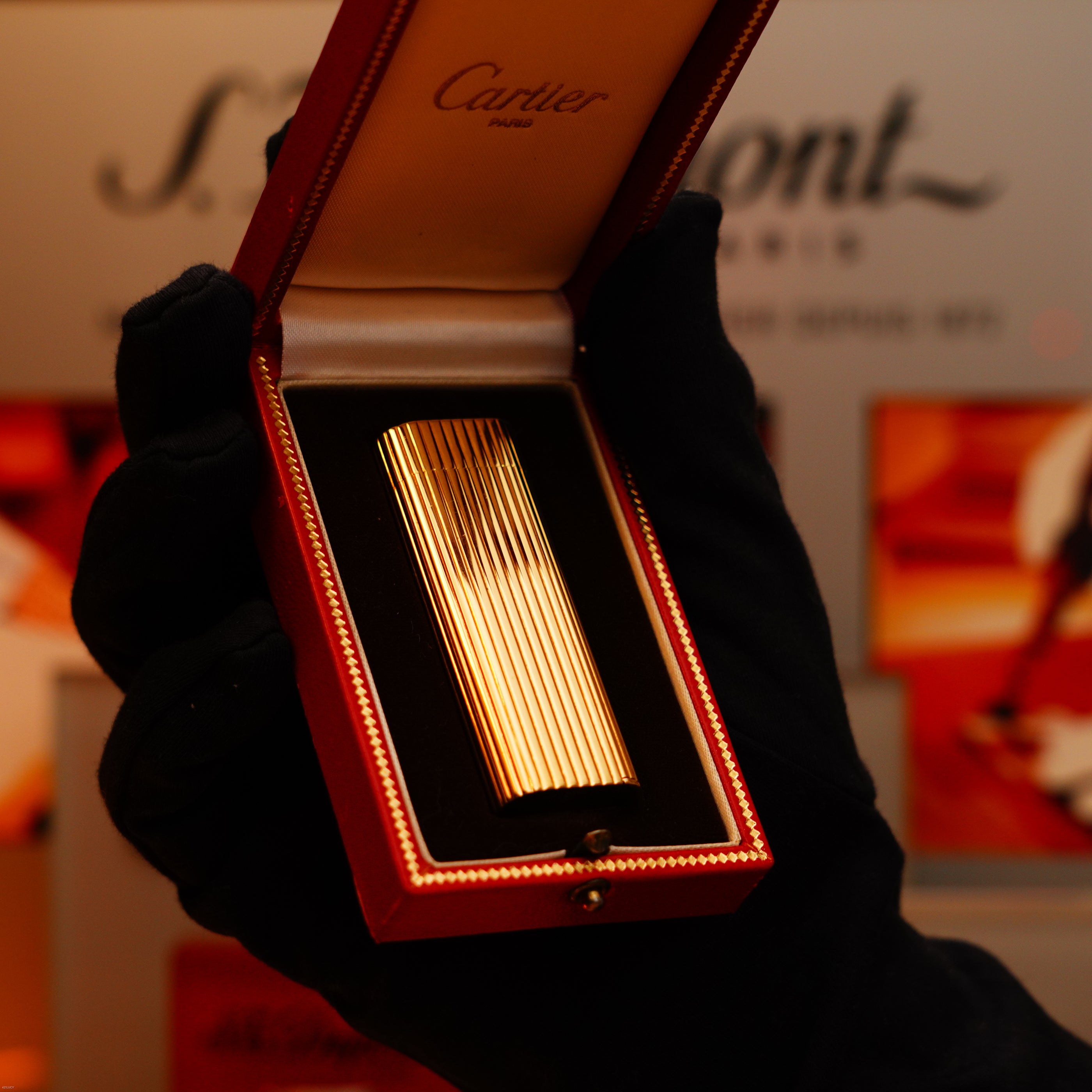 A gloved hand holds an open red Cartier box displaying a Vintage 1970 Extremely Rare Cartier Solid 18k Gold Vertical Line Heavy Lighter with 750 hallmarks, available from KirbyAllison.com.