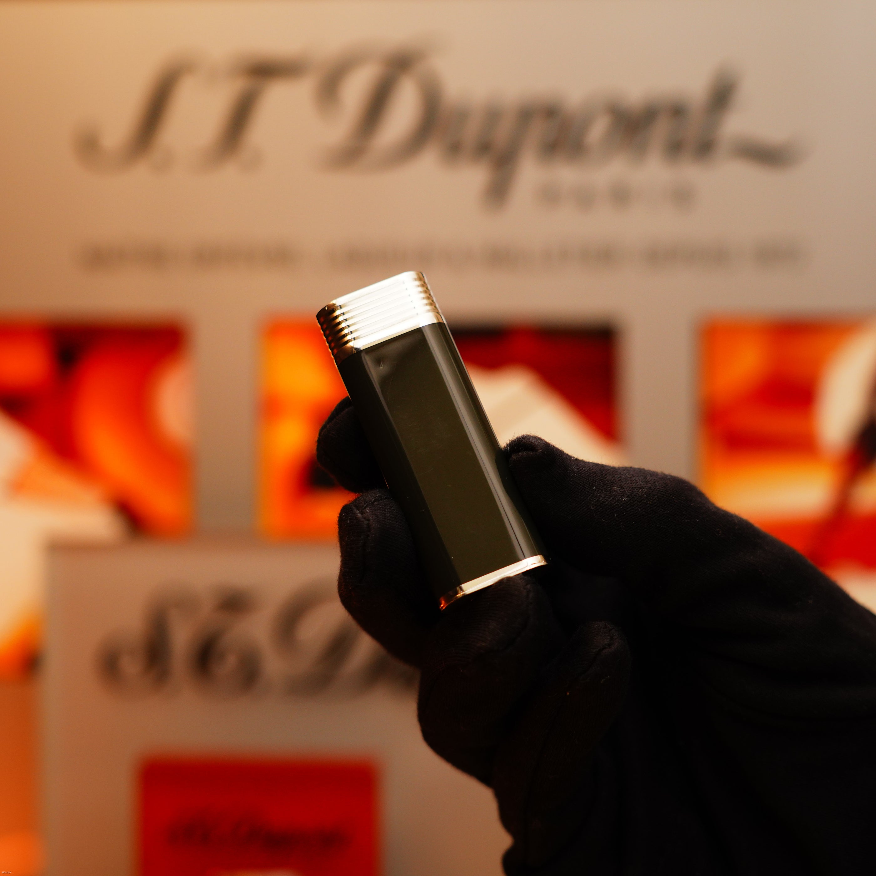 A gloved hand holds a Vintage 1970 Extremely Rare Cartier Solid 925 Sterling Silver Natural Full Dark Green Lacquer Rare Lighter from KirbyAllison.com in front of a blurred S.T. Dupont display.