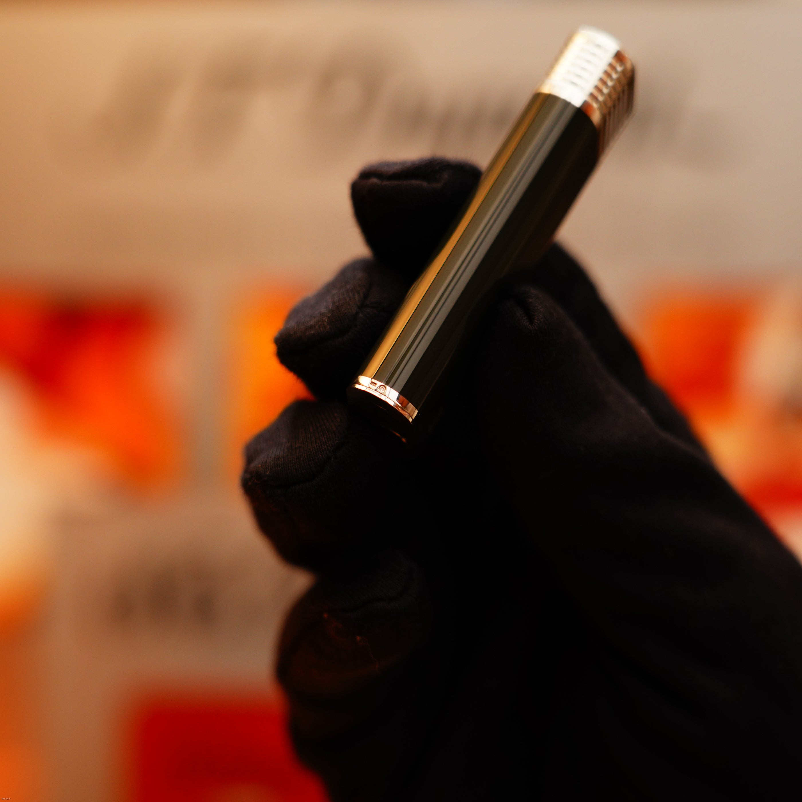 A gloved hand holds the extremely rare Vintage 1970 Cartier Solid 925 Sterling Silver Natural Full Dark Green Lacquer Lighter from KirbyAllison.com against a blurred, warm-toned background.