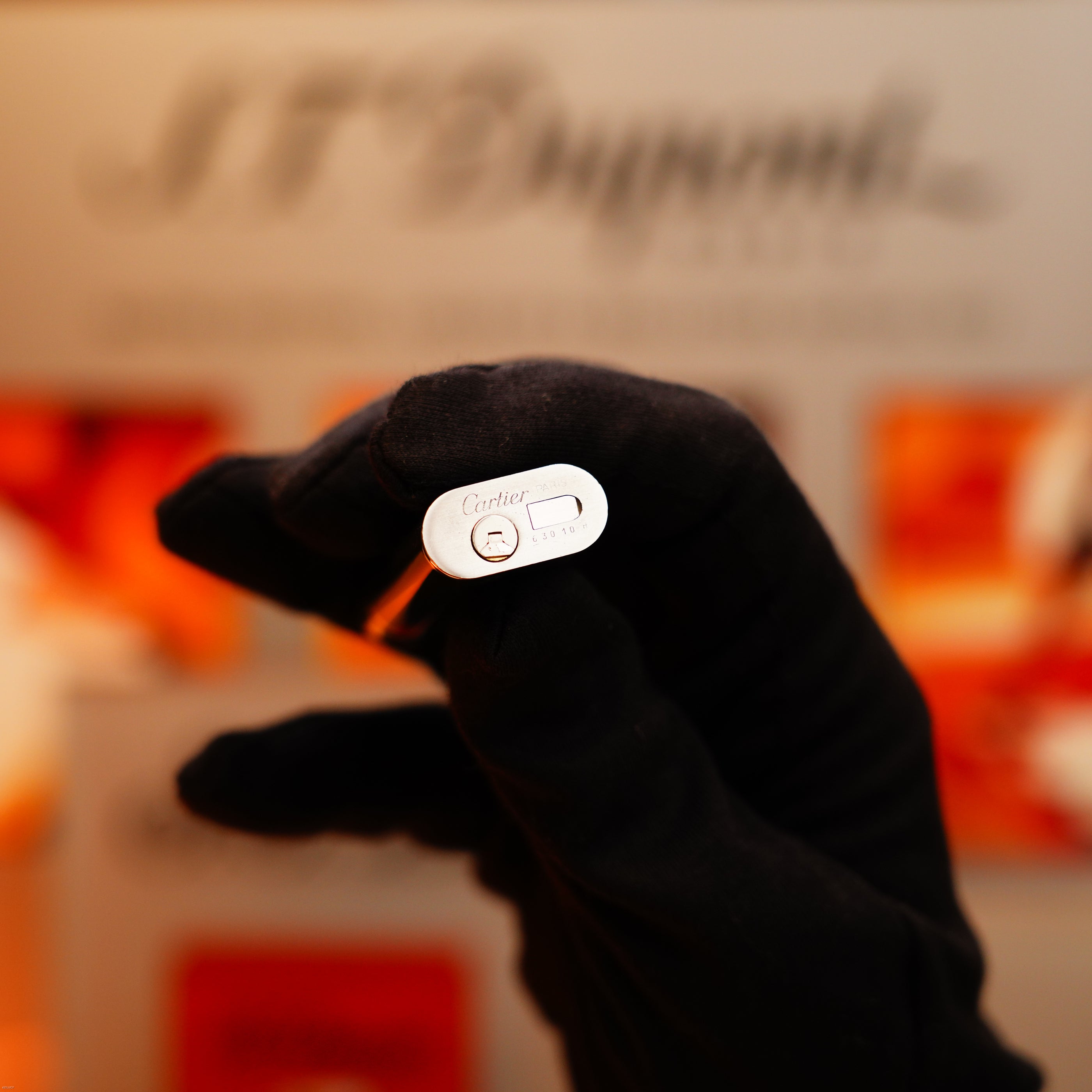 A gloved hand holds a Vintage 1970 Extremely Rare Cartier Solid 925 Sterling Silver Natural Full Dark Green Lacquer Lighter from KirbyAllison.com, engraved with "Cartier" and serial numbers, against a blurred background.