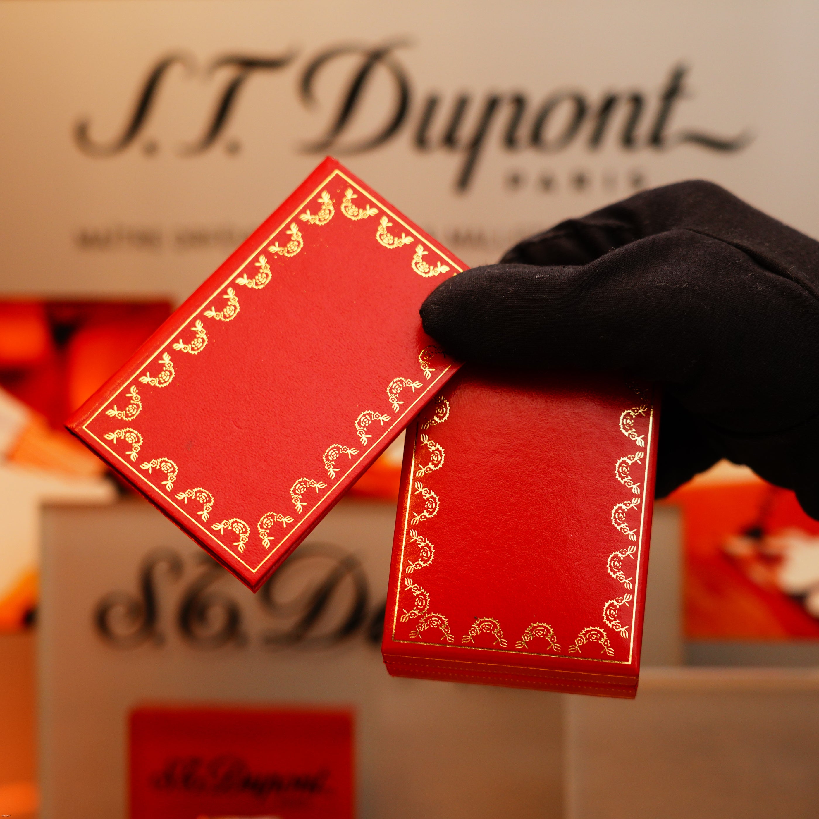 A gloved hand holds two ornate red and gold rectangular boxes in front of a KirbyAllison.com display featuring the Vintage 1970 Extremely Rare Cartier Solid 925 Sterling Silver Natural Full Dark Green Lacquer Rare Lighter.