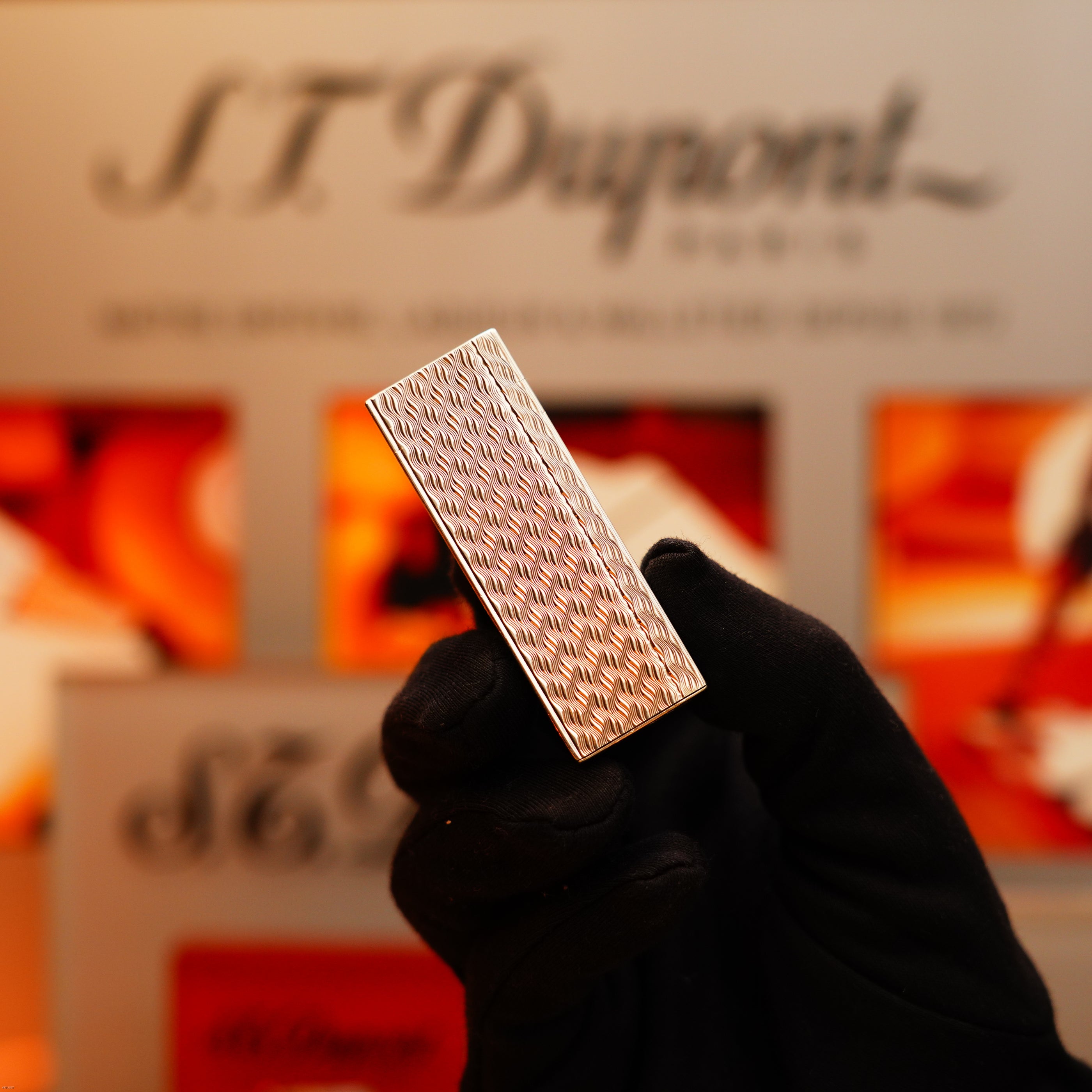 A gloved hand holds a textured Vintage 1970 Early Cartier Production Pentagone Solid 925 Extremely Heavy Sterling Silver Lighter by Cartier in front of a blurred branded display.