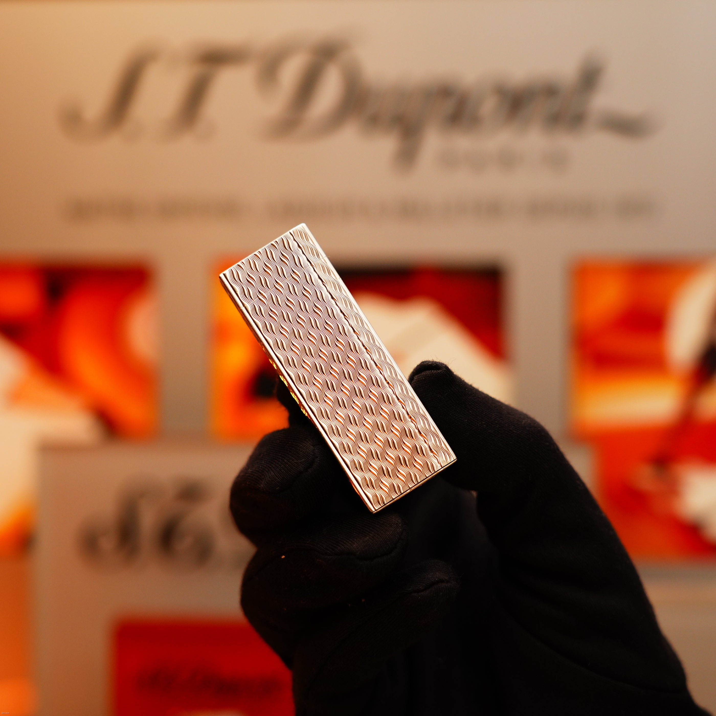 A gloved hand holds a Vintage 1970 Early Cartier Production Pentagone Solid 925 Sterling Silver Lighter by Cartier in front of a blurred display.