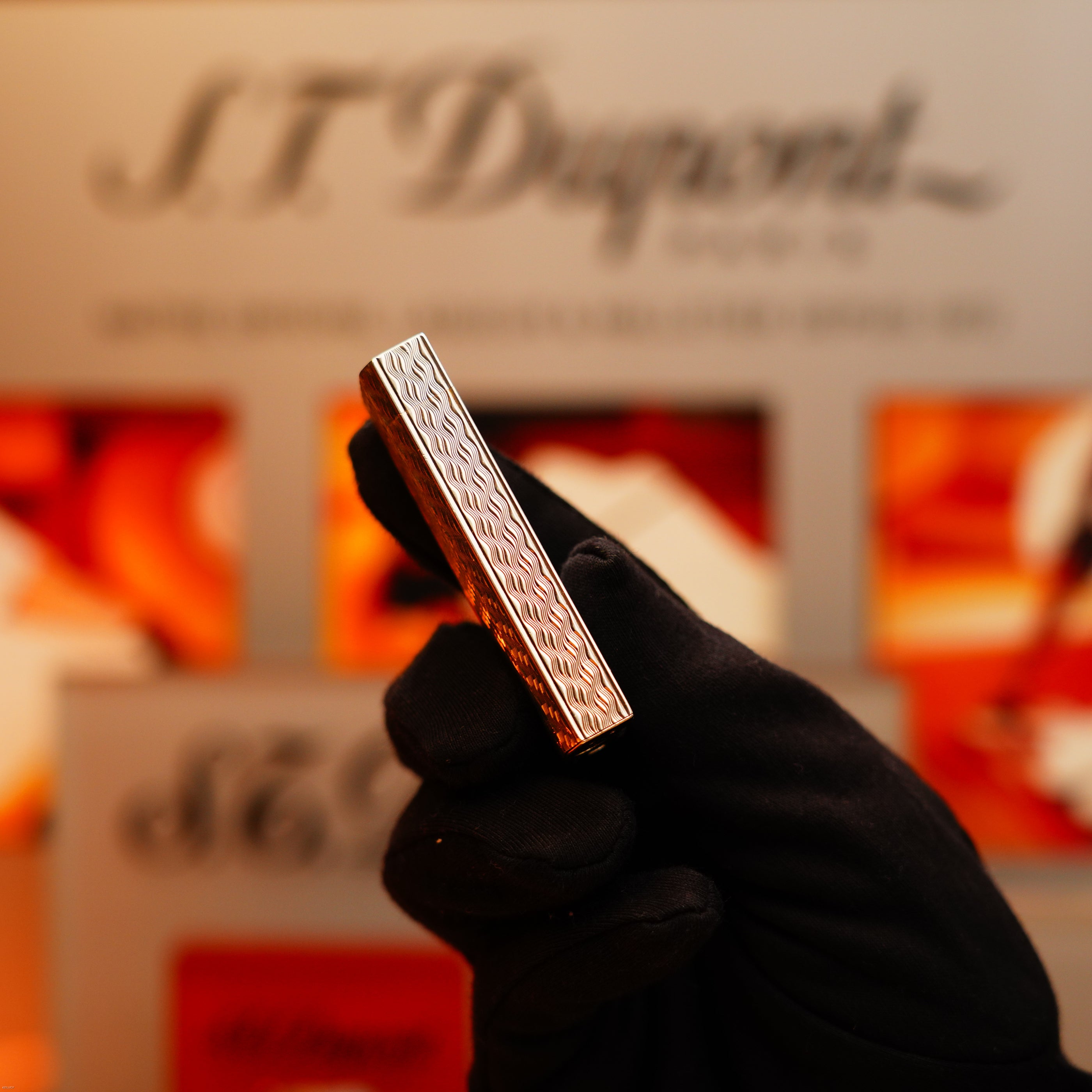 A gloved hand holds a Vintage 1970 Early Cartier Production Pentagone Solid 925 Extremely Heavy Sterling Silver Lighter by Cartier, with a blurred display background.