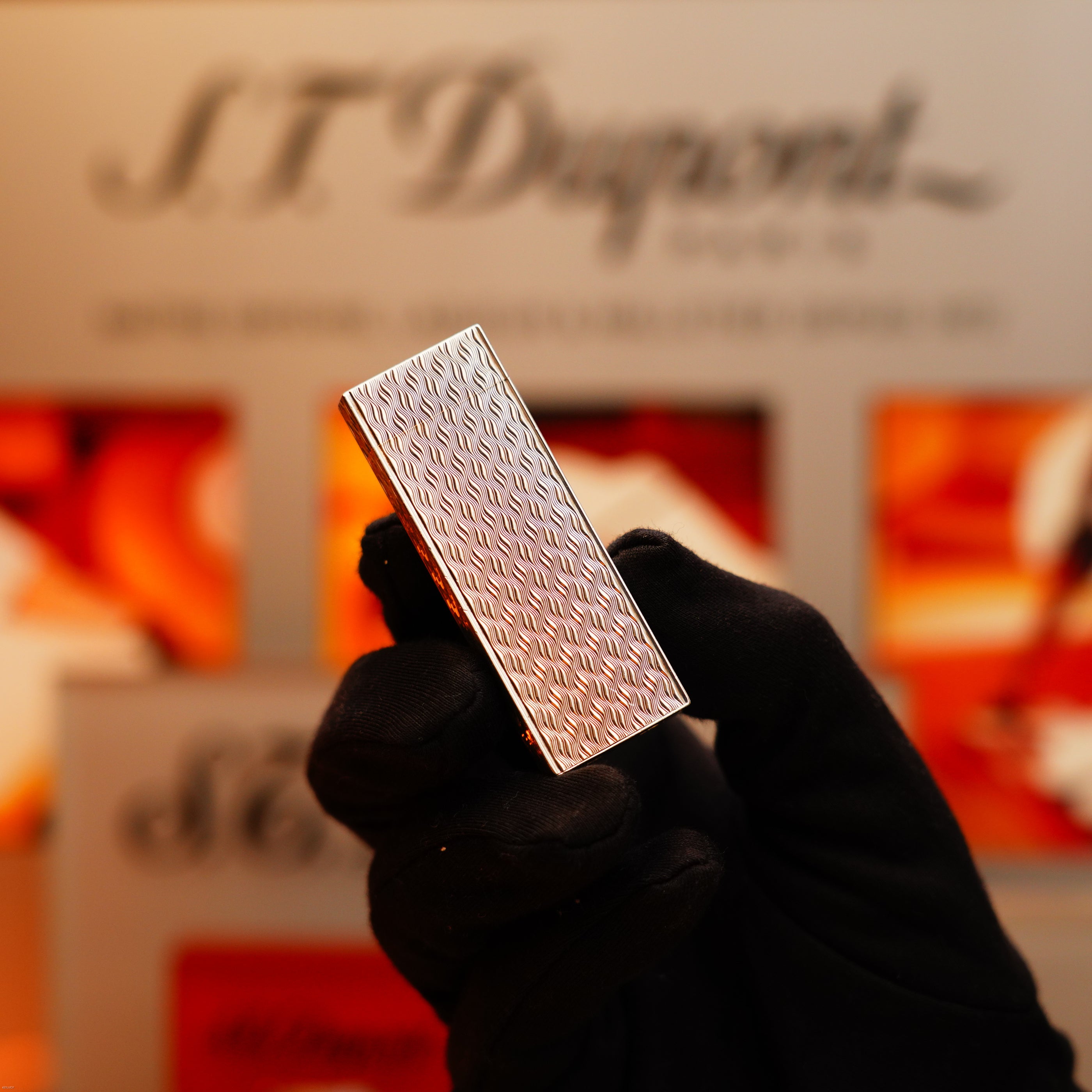 A gloved hand holds a pentagonal, solid 925 extremely heavy sterling silver Vintage 1970 Early Cartier Production lighter, with a blurred Cartier display in the background.
