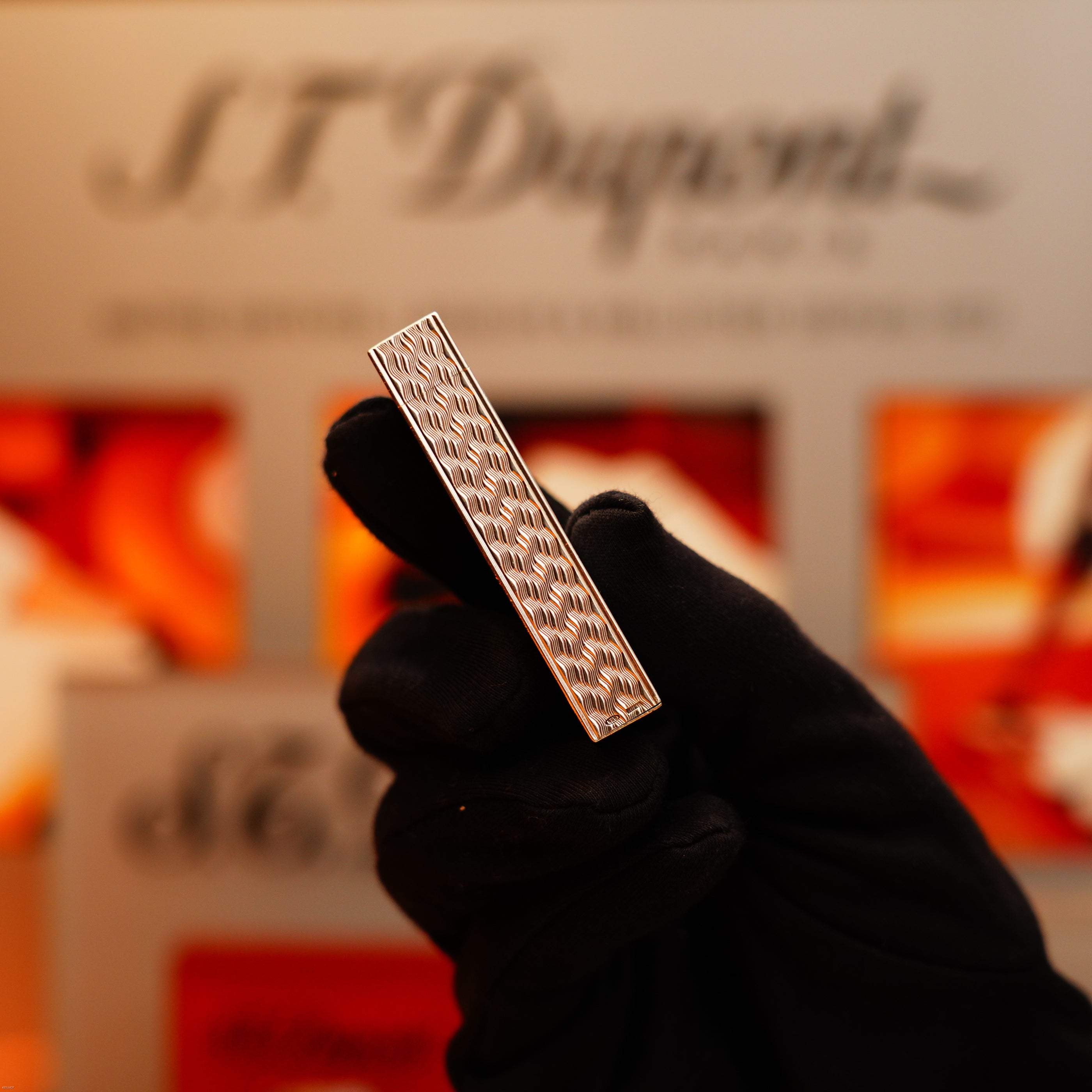 A gloved hand holds a Vintage 1970 Cartier Pentagone Solid 925 Heavy Sterling Silver Lighter with a textured pattern, against a blurred background.