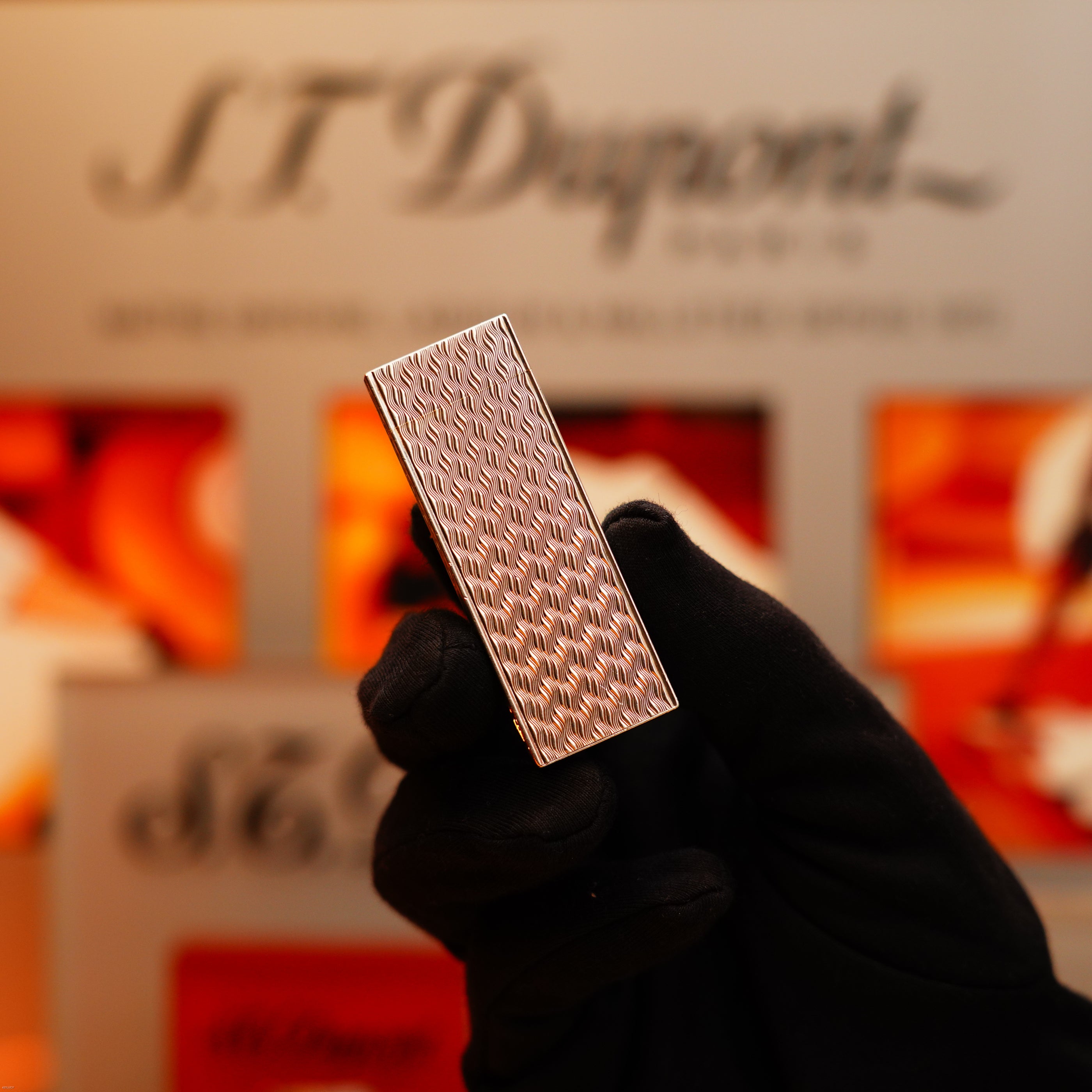 A gloved hand holds a Vintage 1970 Early Cartier Production Pentagone Solid 925 Heavy Sterling Silver Lighter by Cartier, with a blurred S.T. Dupont display in the background.
