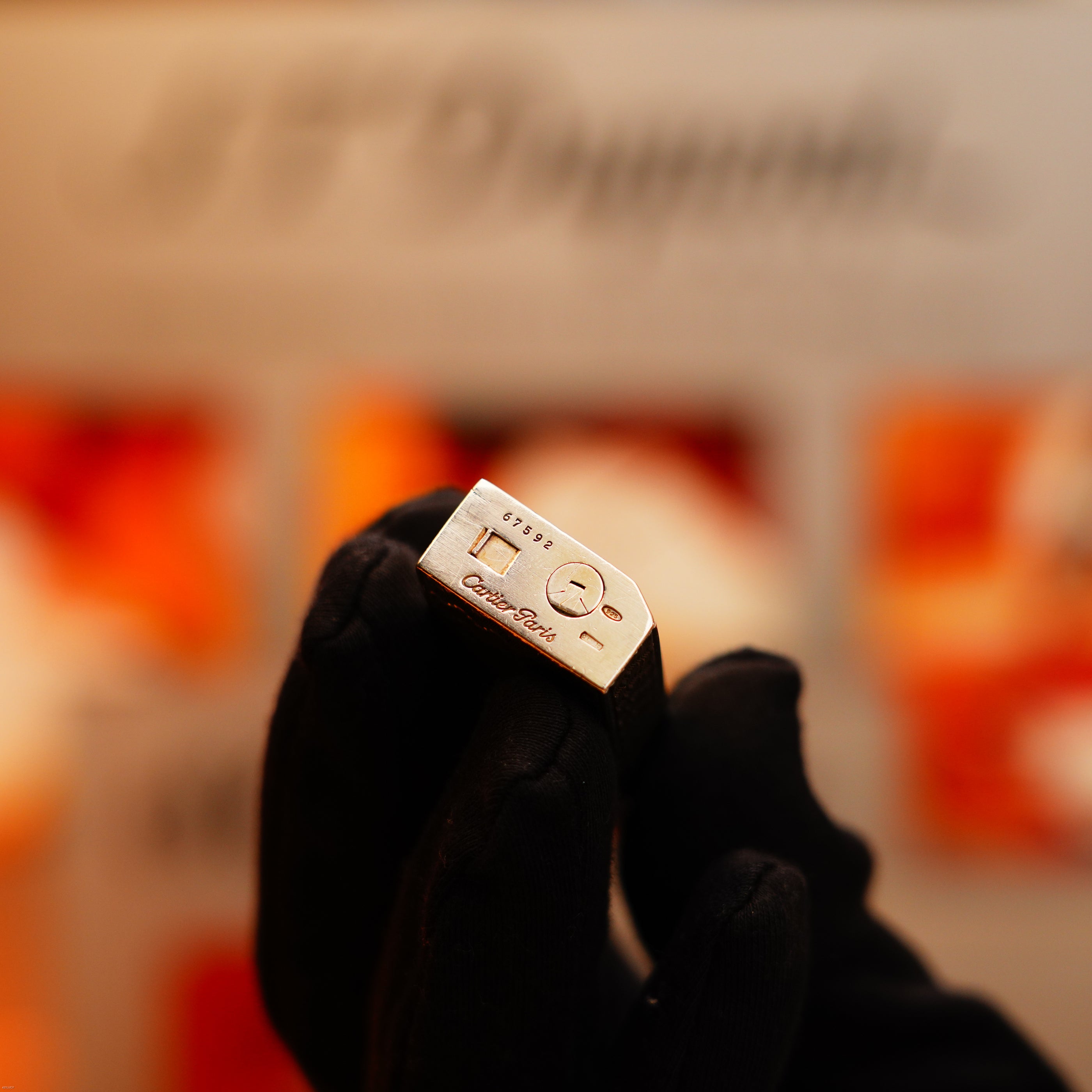 A gloved hand holds a Vintage 1970 Early Cartier Production Pentagone Solid 925 Heavy Sterling Silver Lighter by Cartier, with engraved details, photographed against a blurred background.