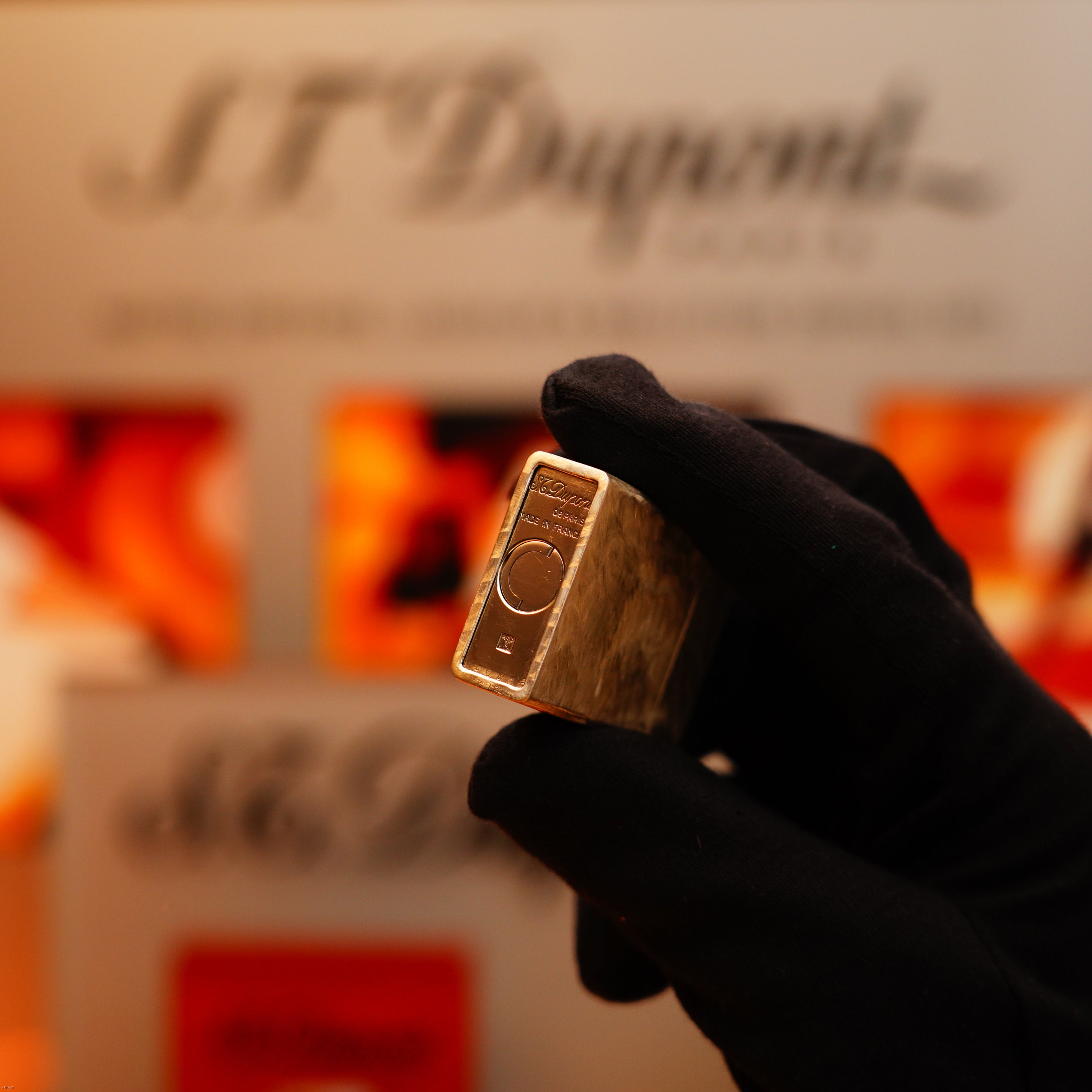 A gloved hand holds a Vintage 1970 de St Dupont Two Tone Solid 925 Sterling Silver Guilloché Pattern Lighter by S.T. Dupont, with blurred branding visible in the background.