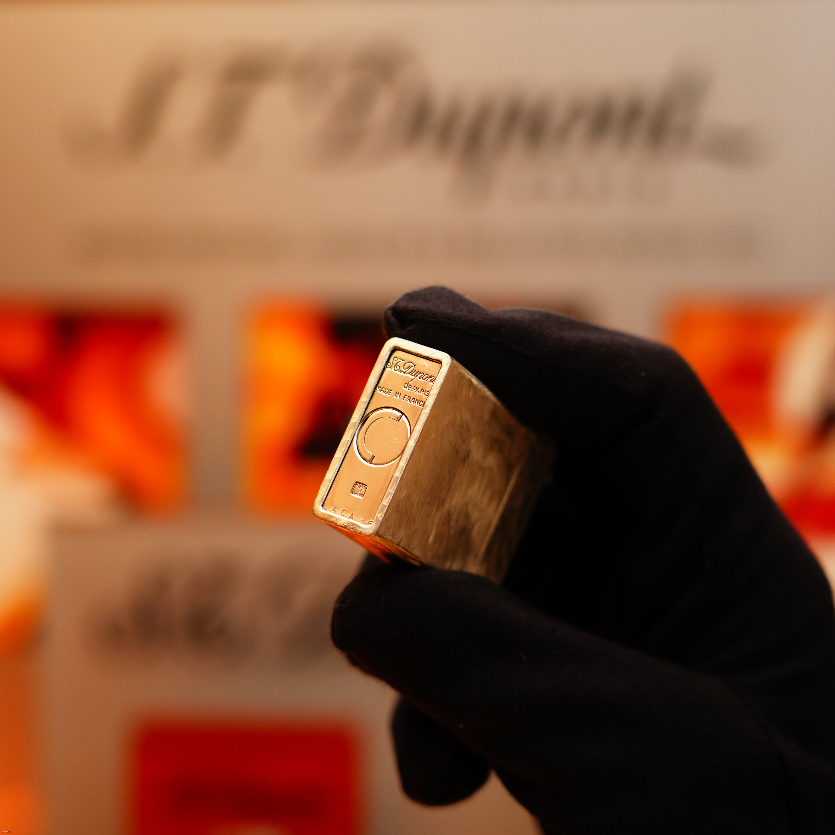 A gloved hand holds a Vintage 1970 S.T. Dupont Two Tone Solid 925 Sterling Silver Guilloché Pattern Lighter before a blurred background with the S.T. Dupont logo.
