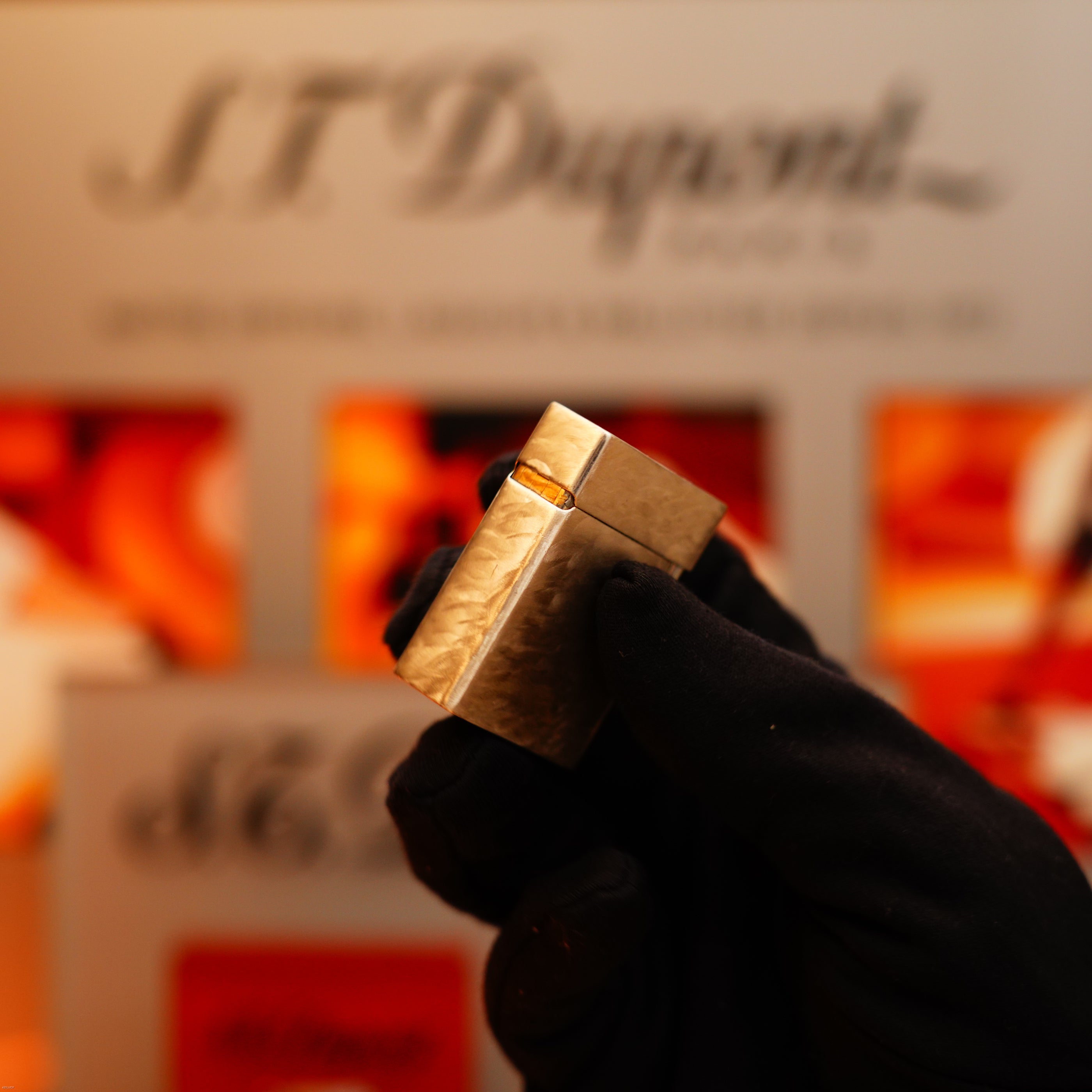 A gloved hand holds a Vintage 1970 S.T. Dupont Two Tone Solid 925 Sterling Silver Guilloché Pattern Lighter in front of a blurred S.T. Dupont display background.